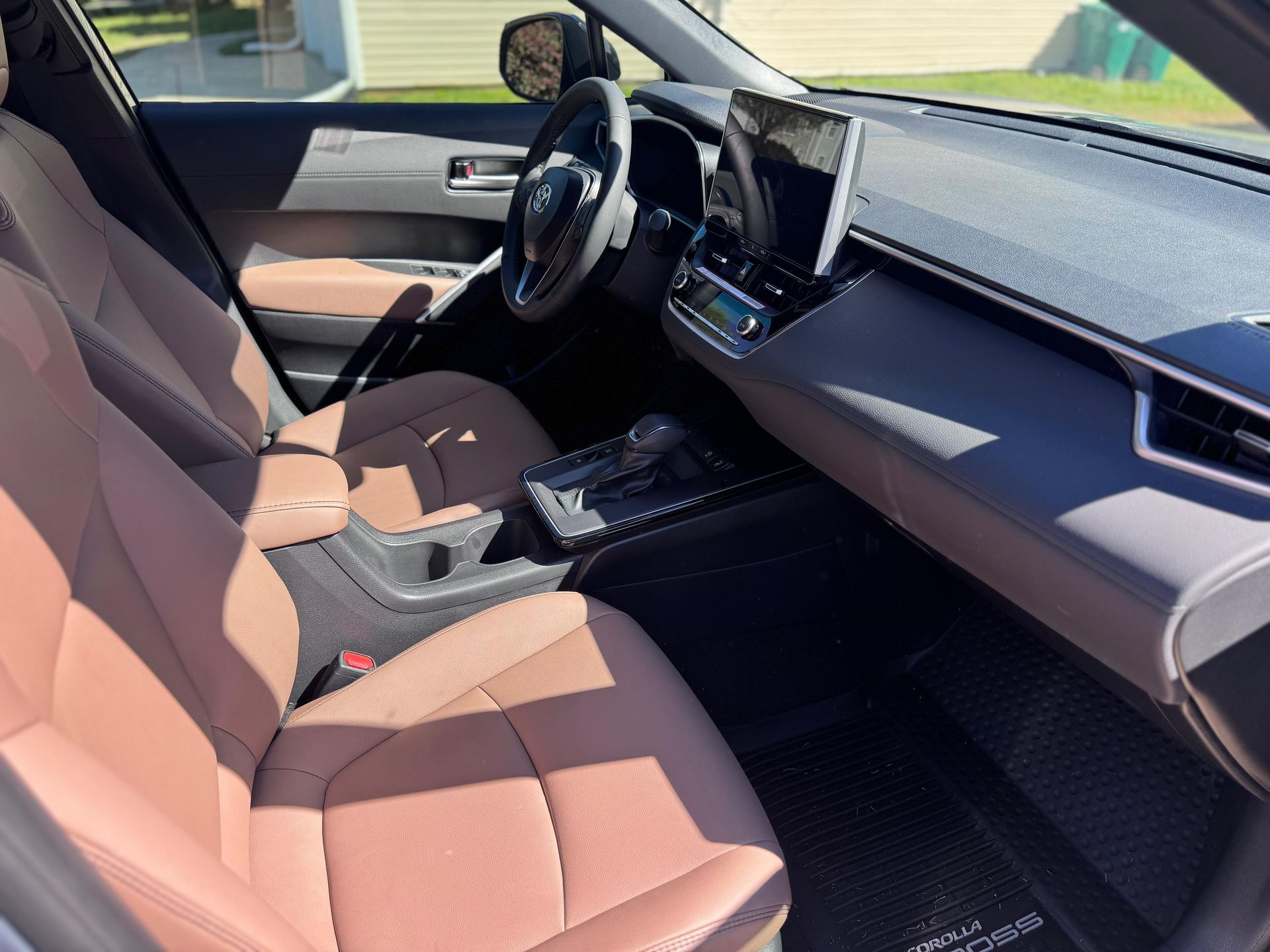 Modern car interior featuring tan upholstered front seats, a digital infotainment screen, and a dark dashboard.