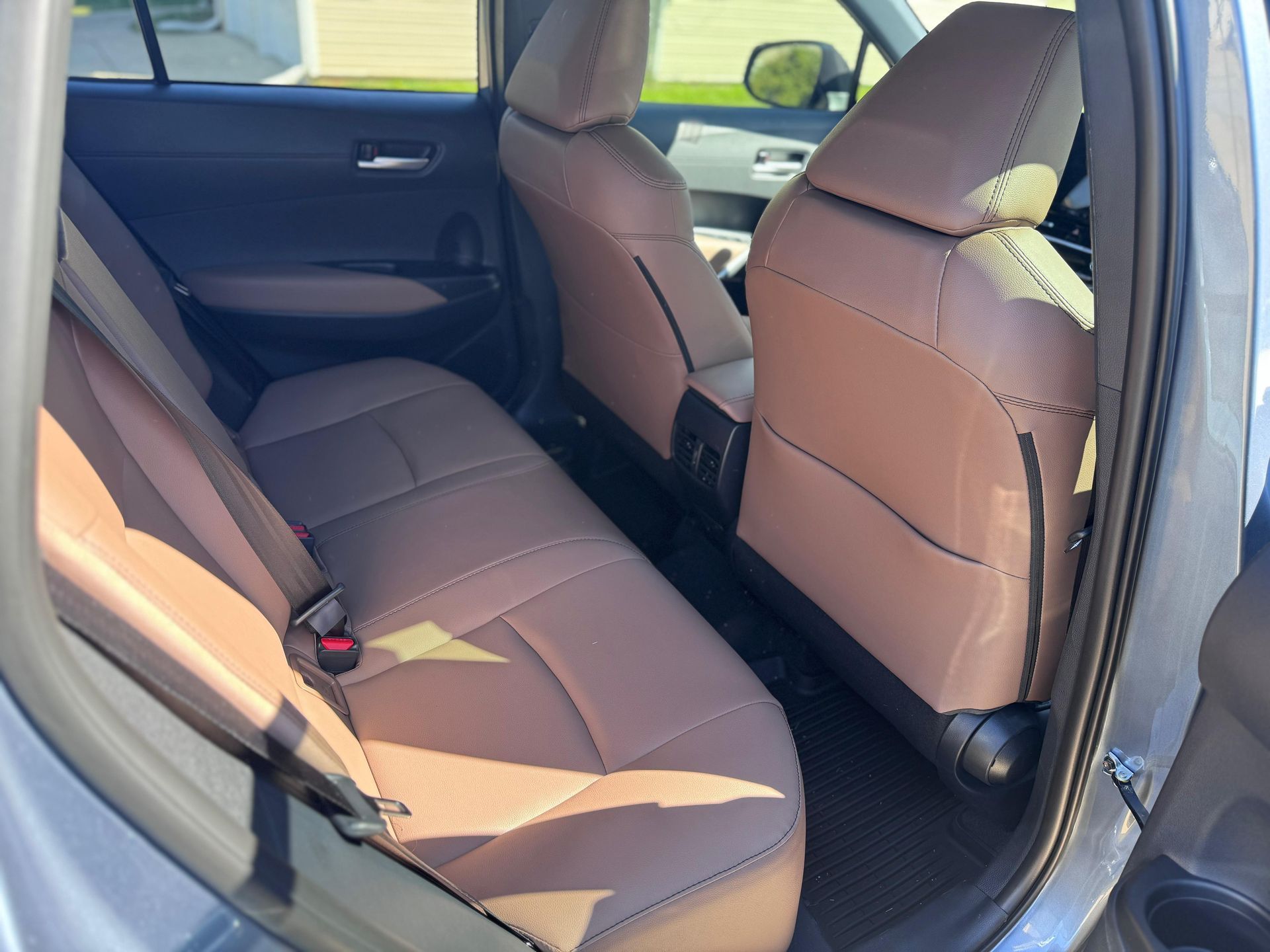 Interior view of a vehicle’s back seat with tan leather upholstery and black floor mats.