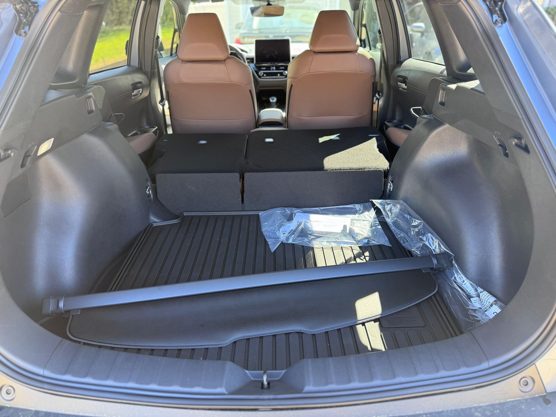 Empty trunk of a car with folded rear seats, tan upholstery, and a black cargo cover lying on a textured rubber floor mat.