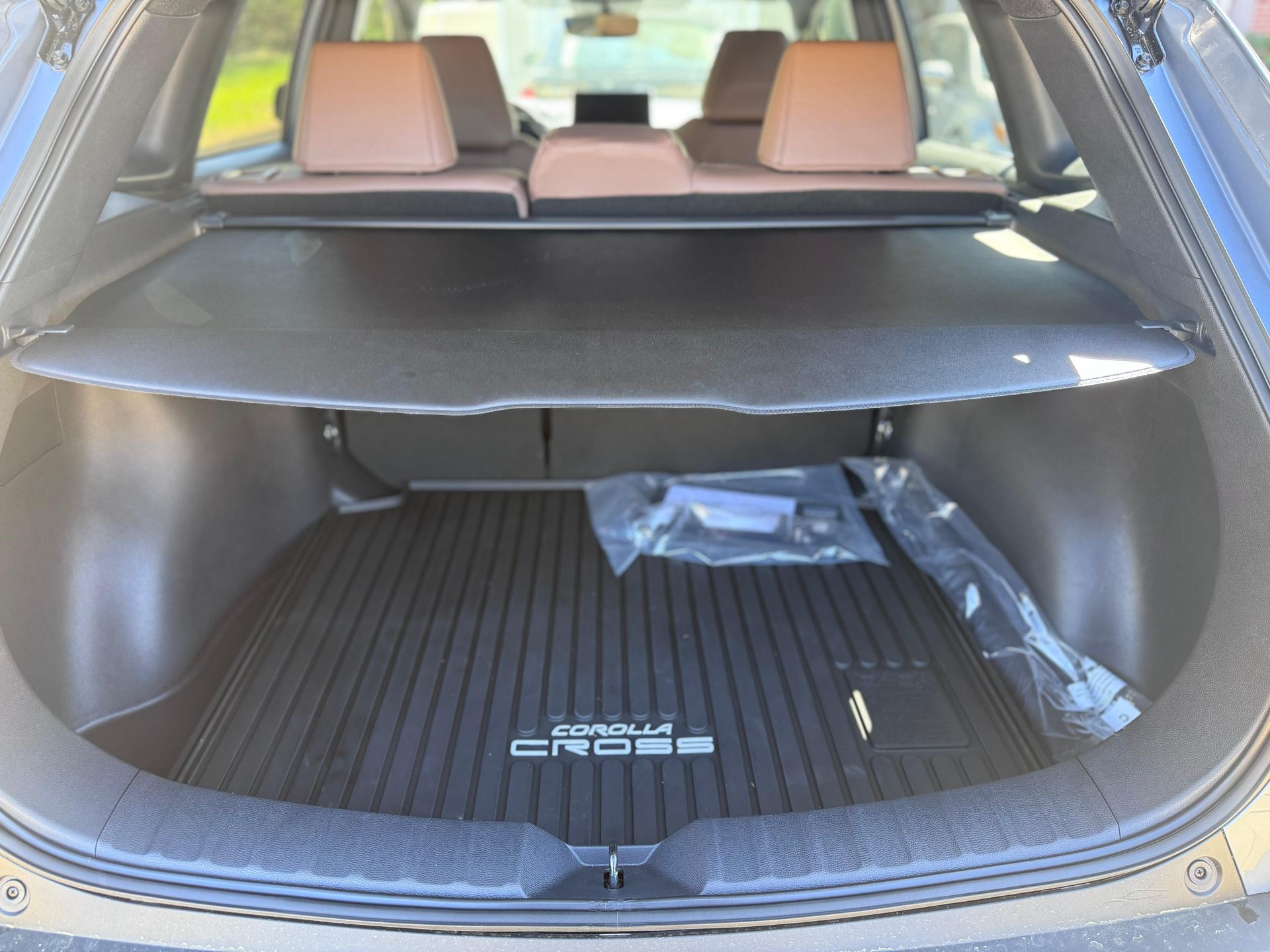 The open trunk of a Corolla Cross vehicle featuring a black cargo mat and a retractable privacy cover.