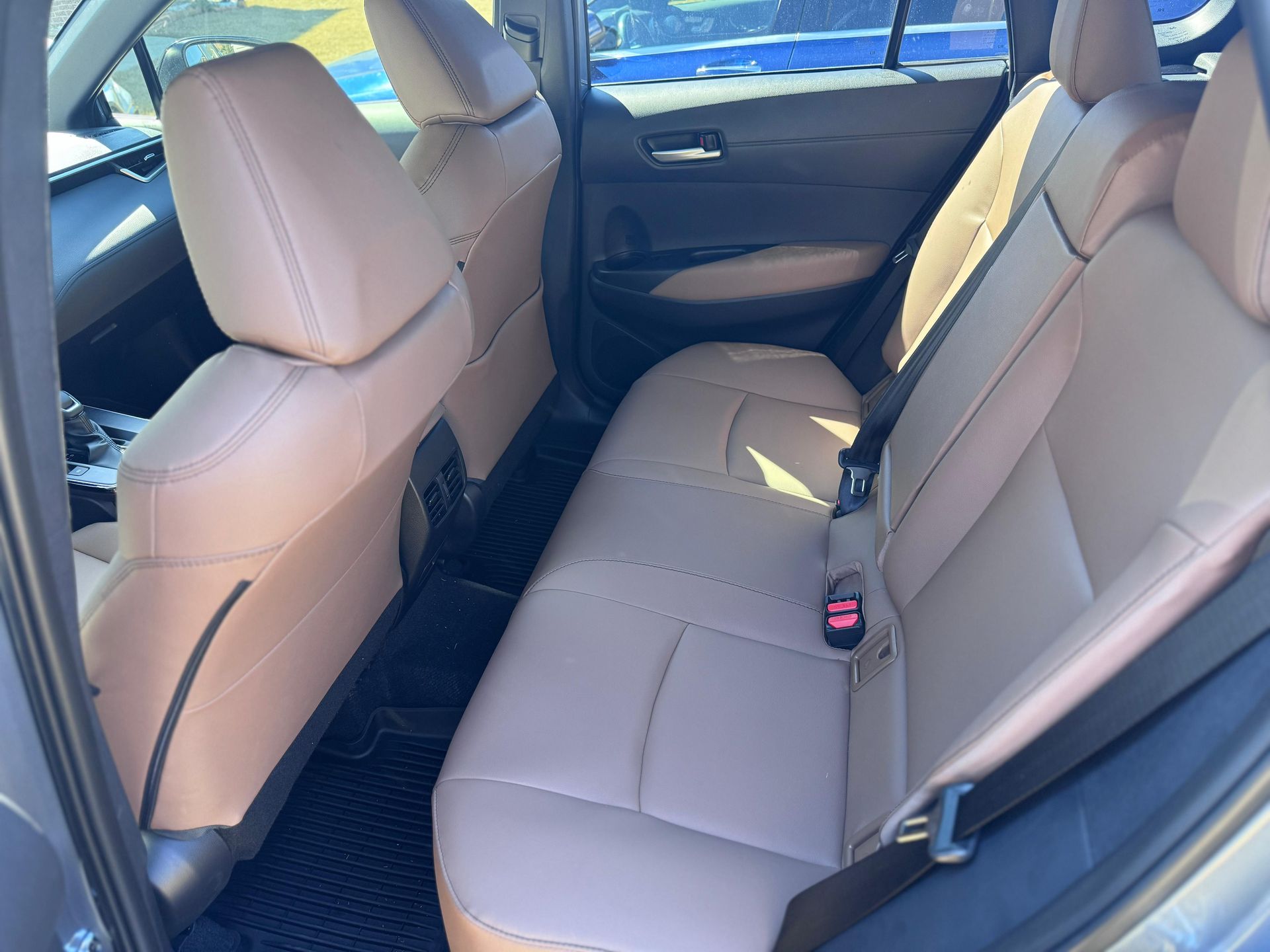 The back interior of a car featuring tan leather seats and dark floor mats.