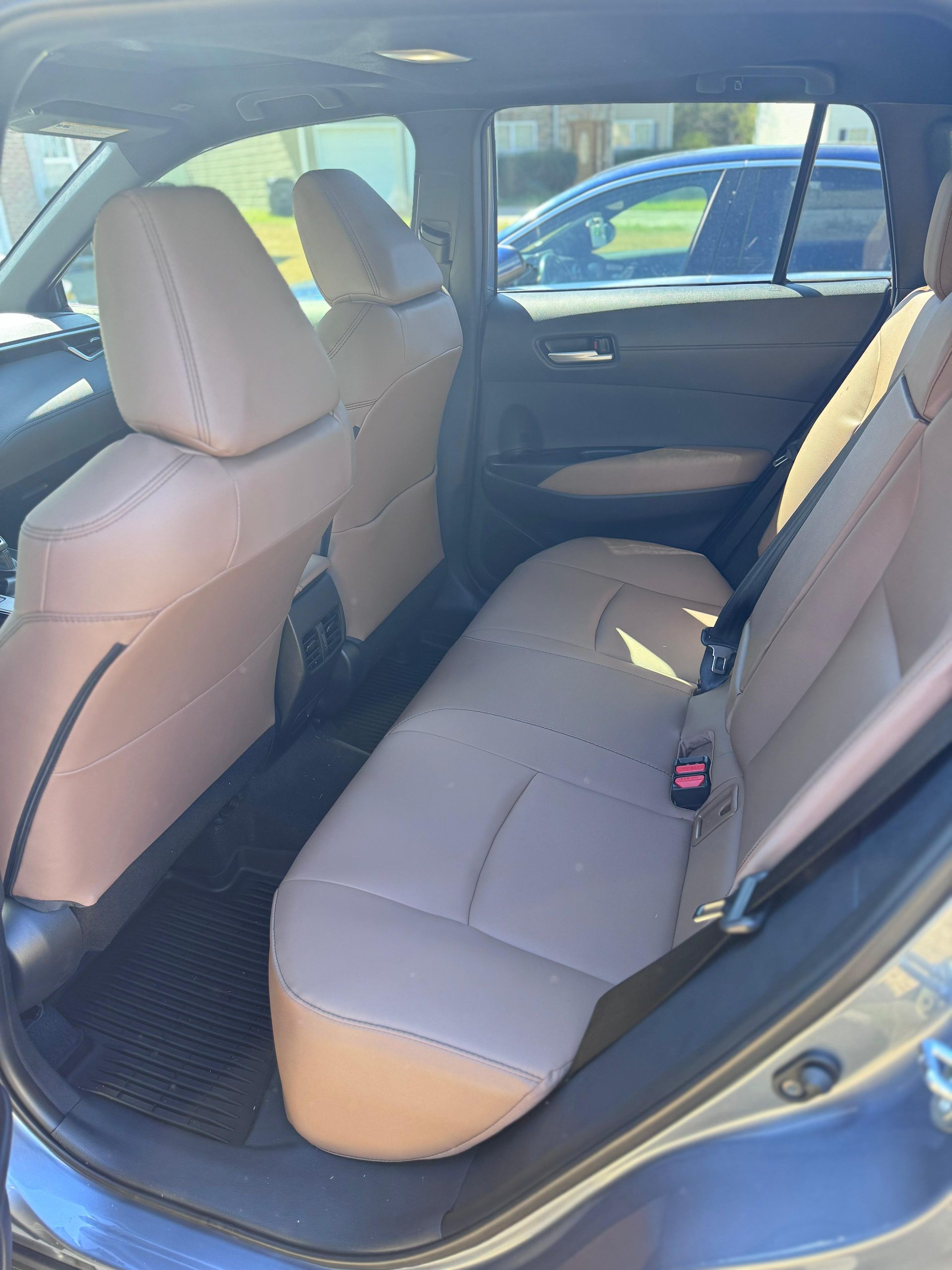 The interior of a car’s back seat features tan leather upholstery, headrests, and black floor mats.