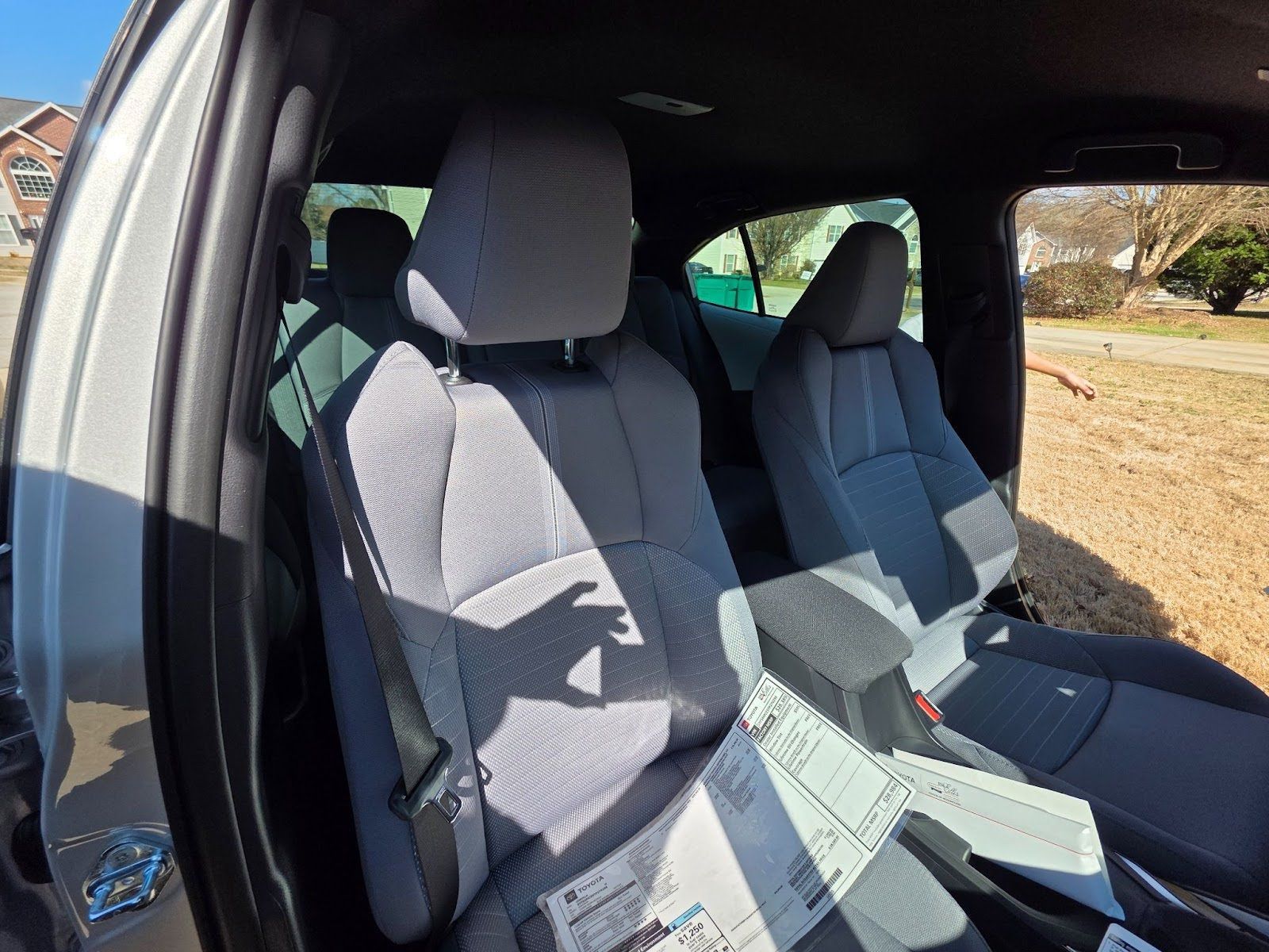 Interior of a vehicle featuring gray fabric front seats, a center console, and paperwork resting on the passenger seat.