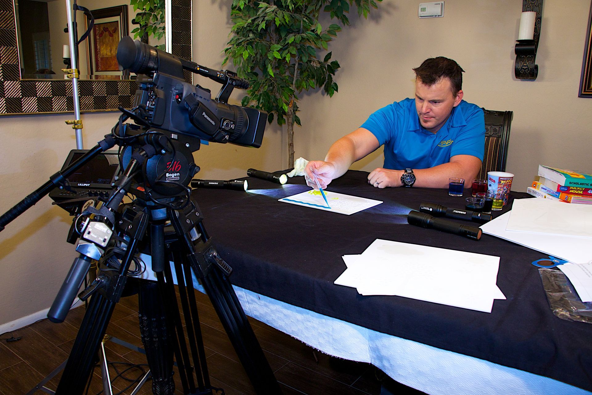 A man in a blue shirt is sitting at a table in front of a camera