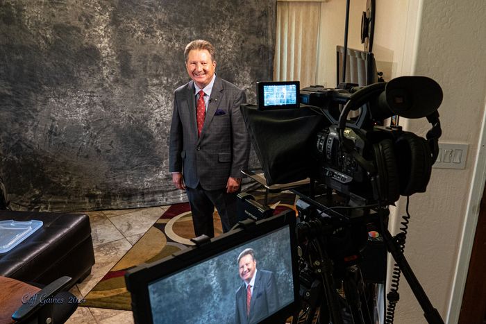 A man in a suit and tie is standing in front of a camera.