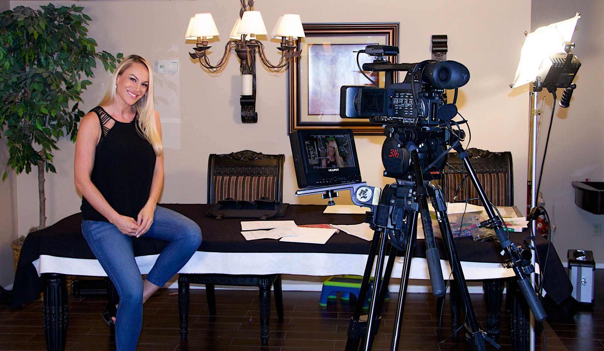 A woman is sitting on a table in front of a camera.