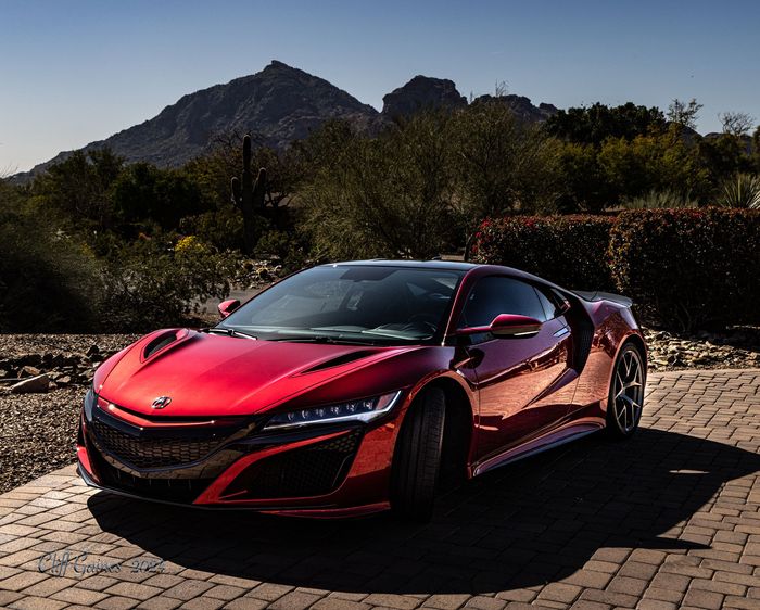 A red sports car is parked in front of a mountain