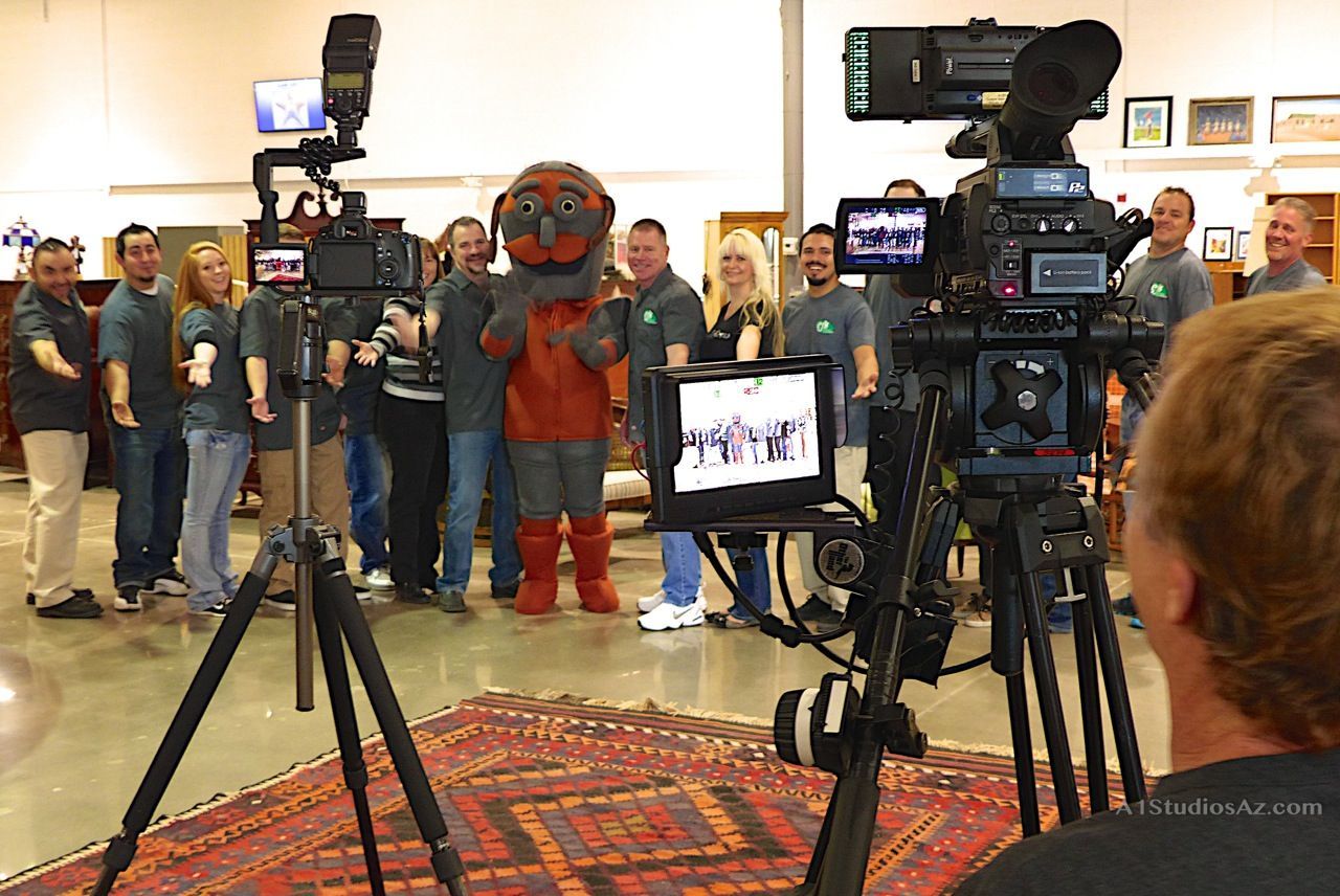 A group of people standing in front of a camera with a mascot in the background