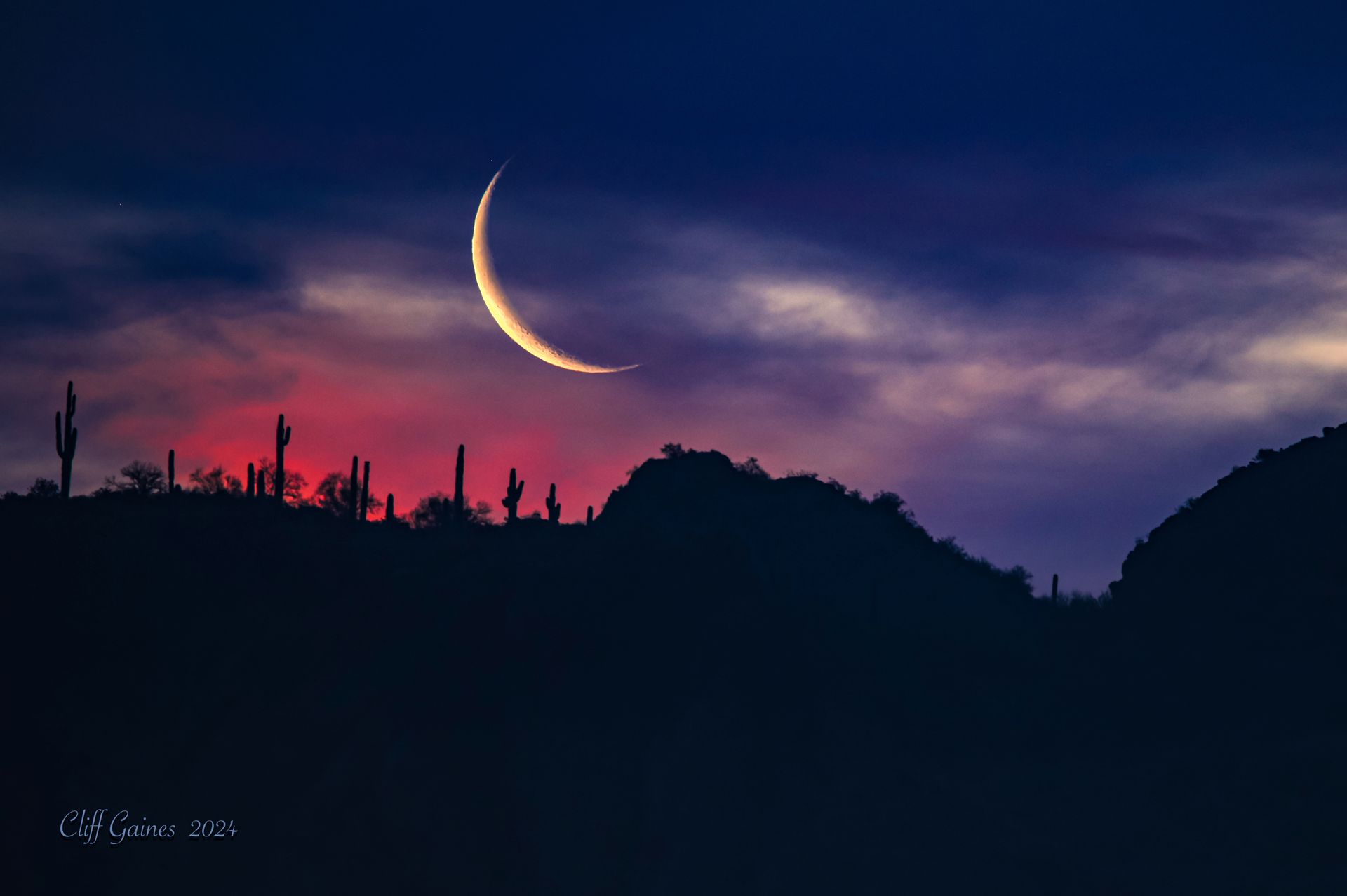 A crescent moon is rising over a mountain range at sunset.