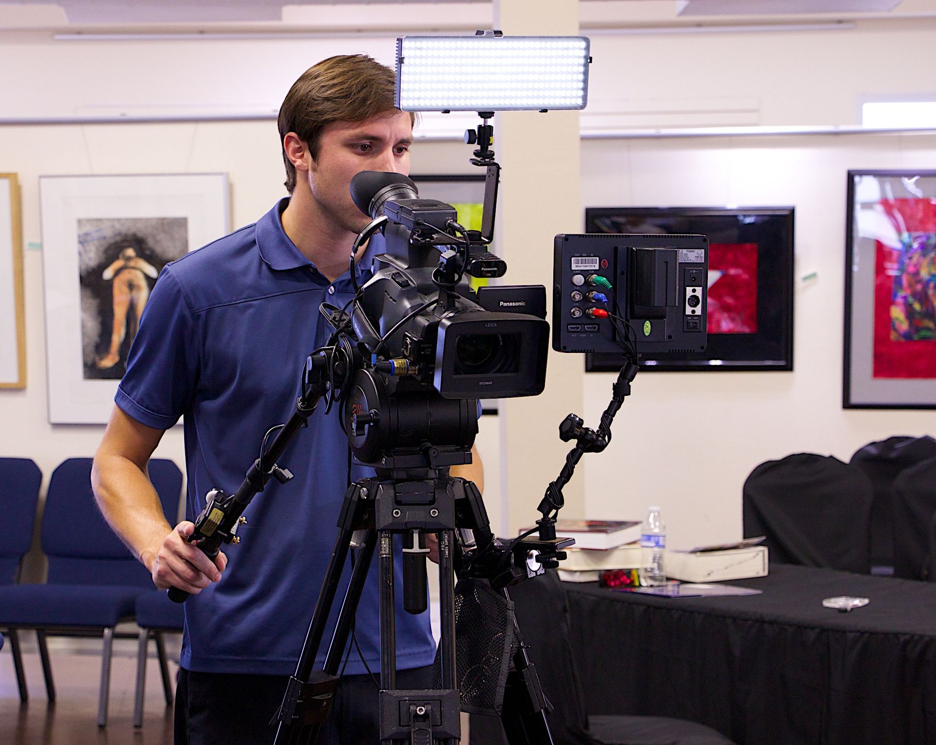 A man in a blue shirt is standing in front of a camera on a tripod