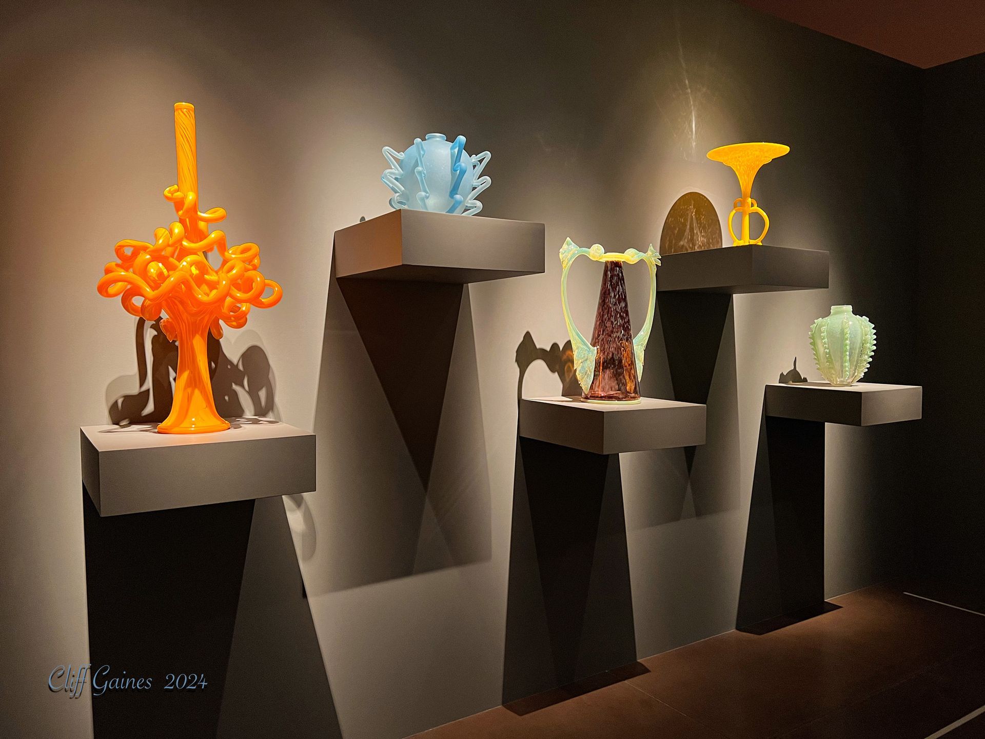 A display of various colored vases on shelves in a dark room