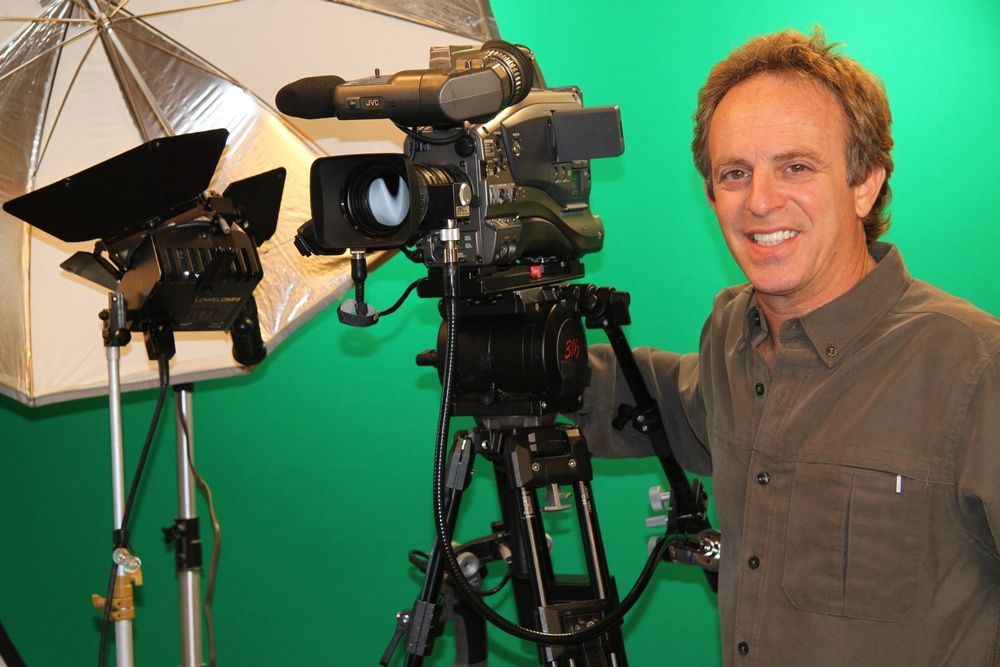 A man standing in front of a green screen with a camera on a tripod