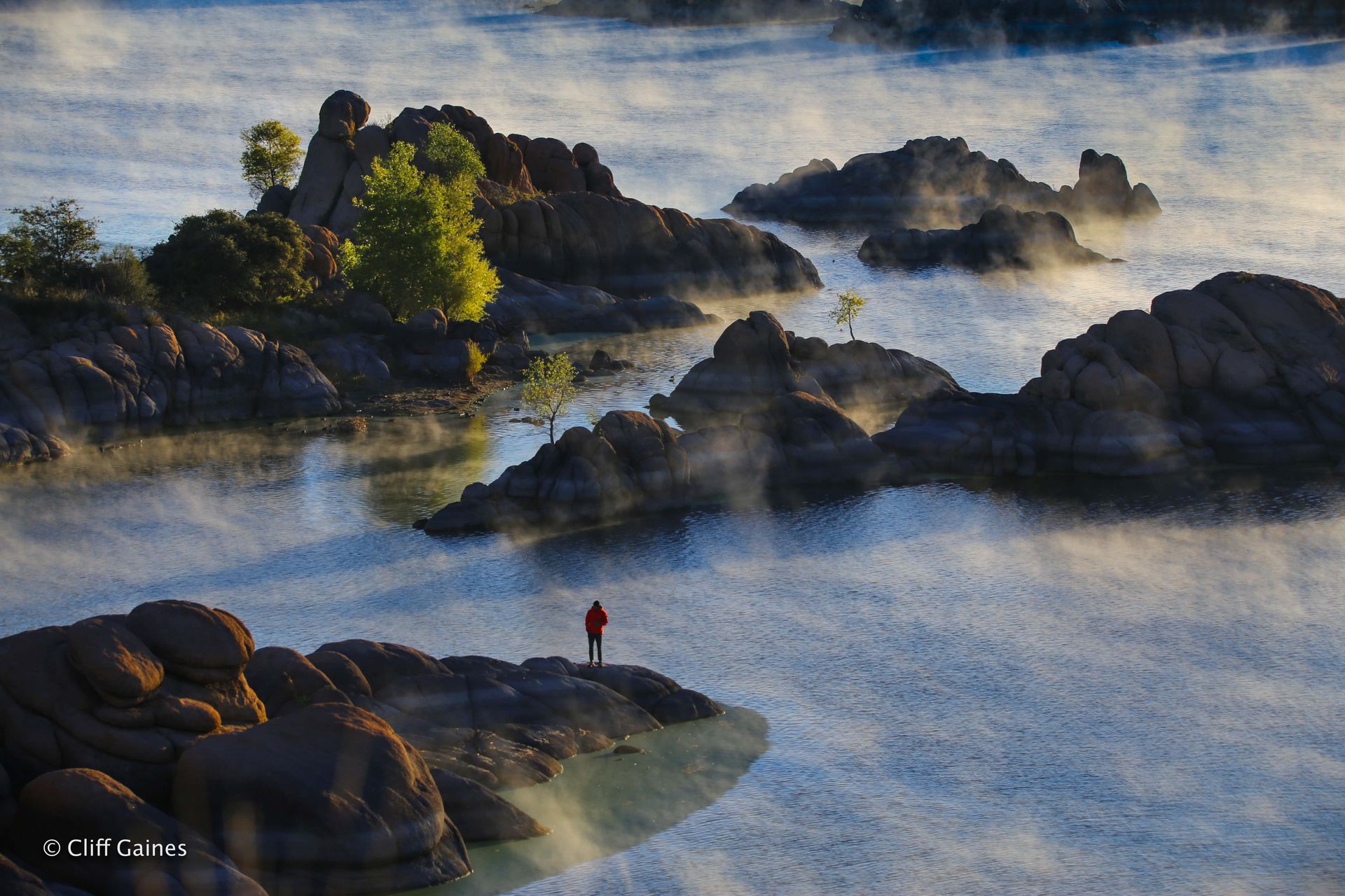 A person is standing on a rock in the middle of a lake.
