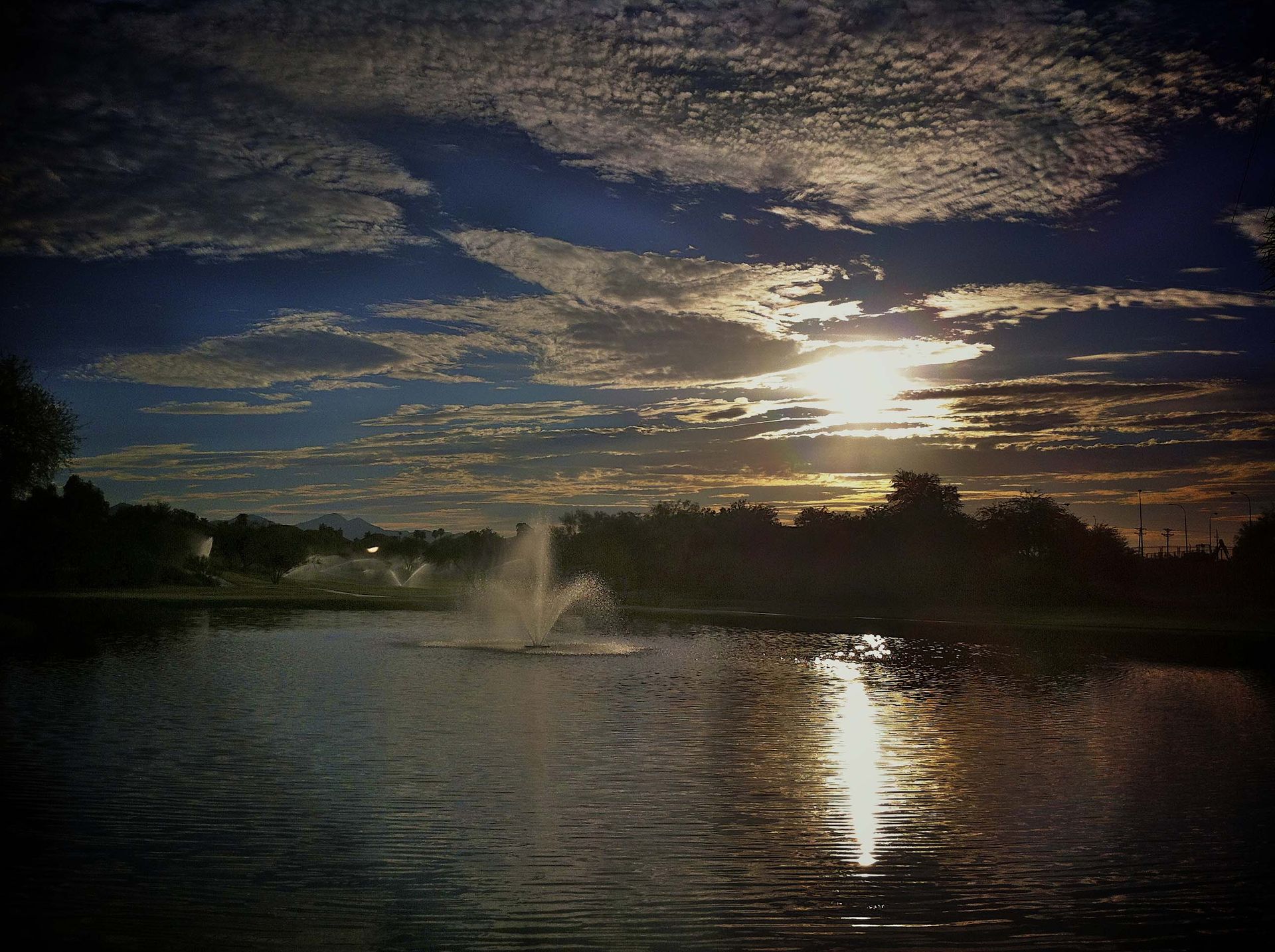 A lake with a fountain in the middle of it at sunset