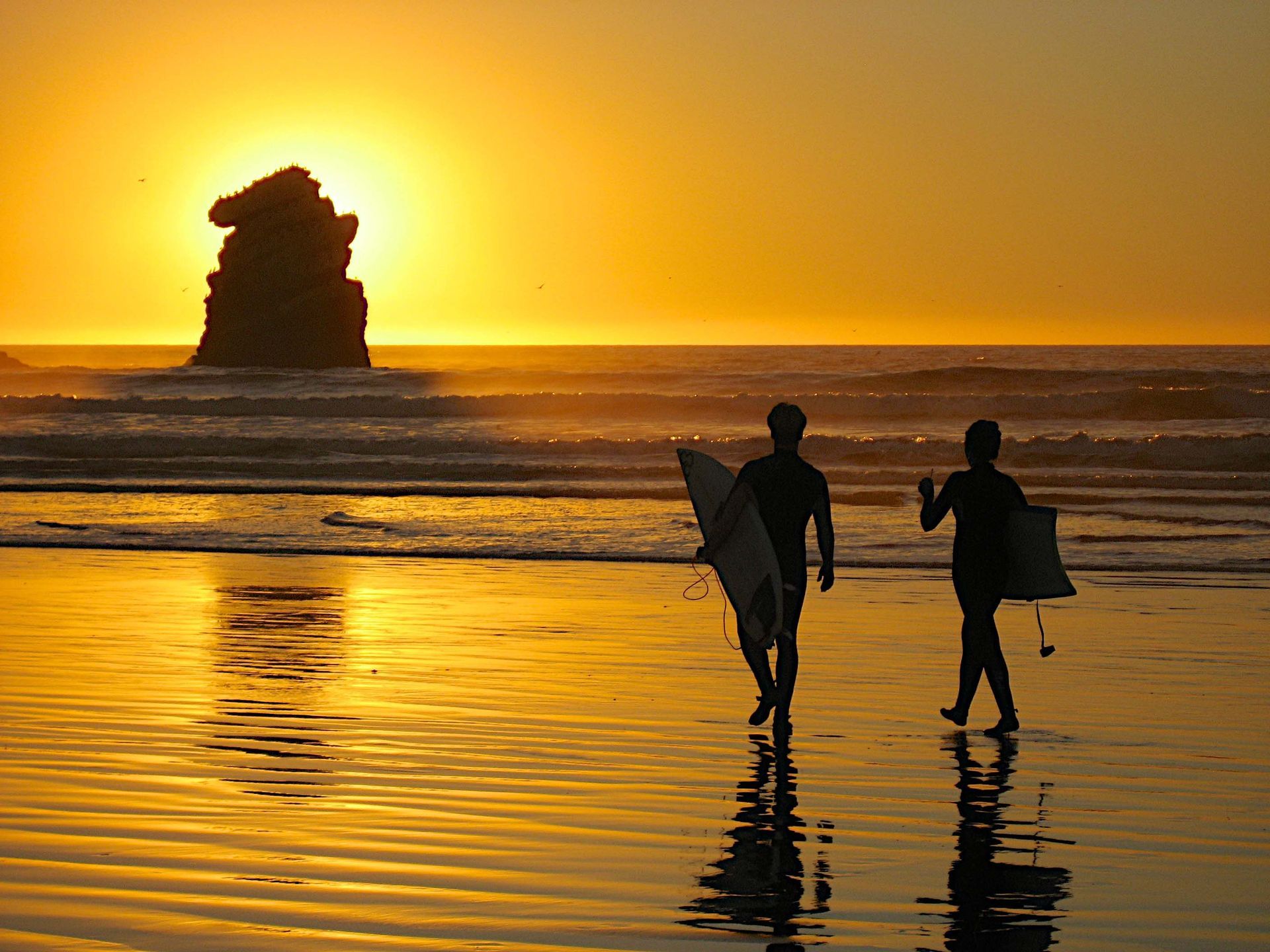 Two surfers are walking on the beach at sunset