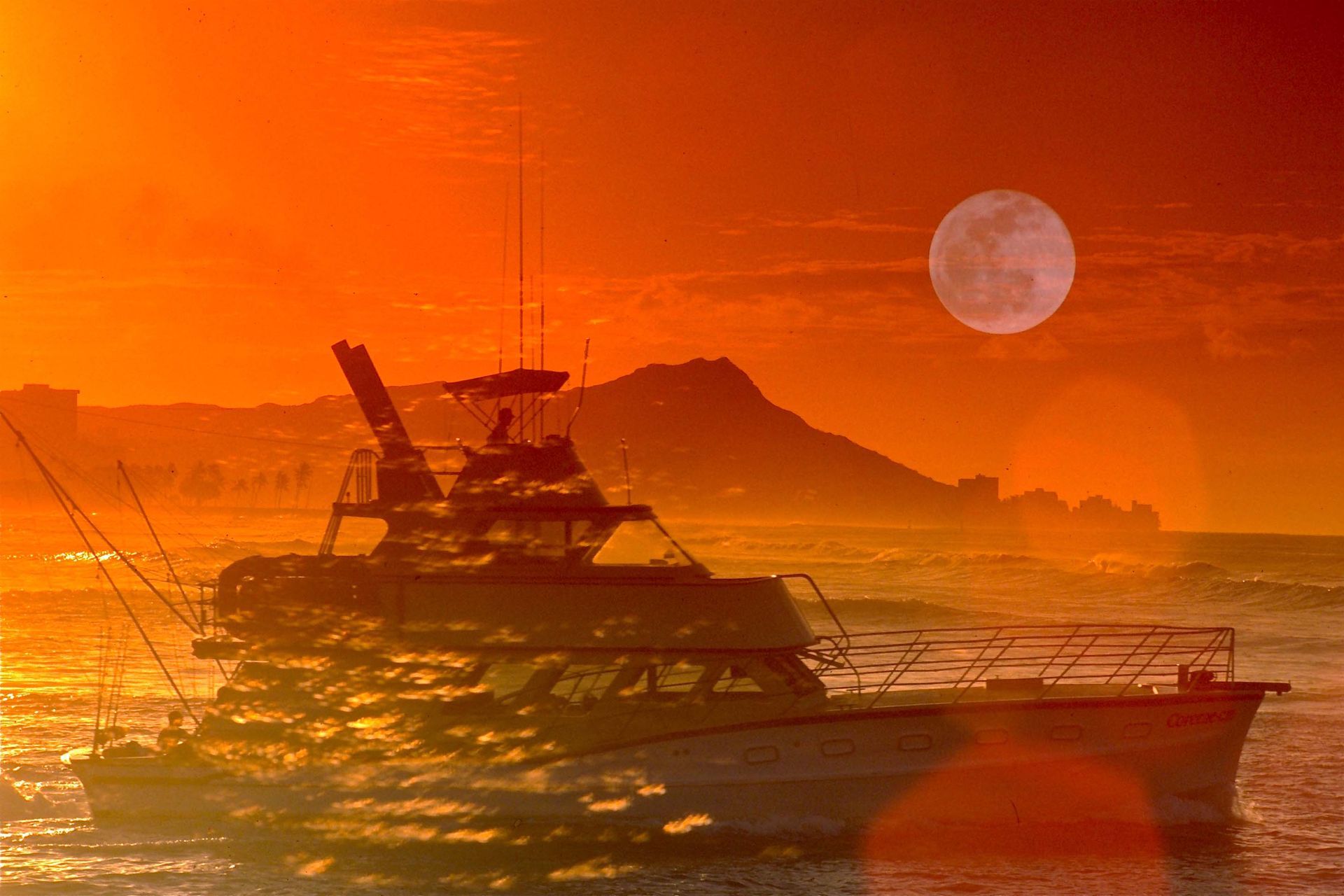 A boat is floating in the ocean at sunset with a full moon in the background.