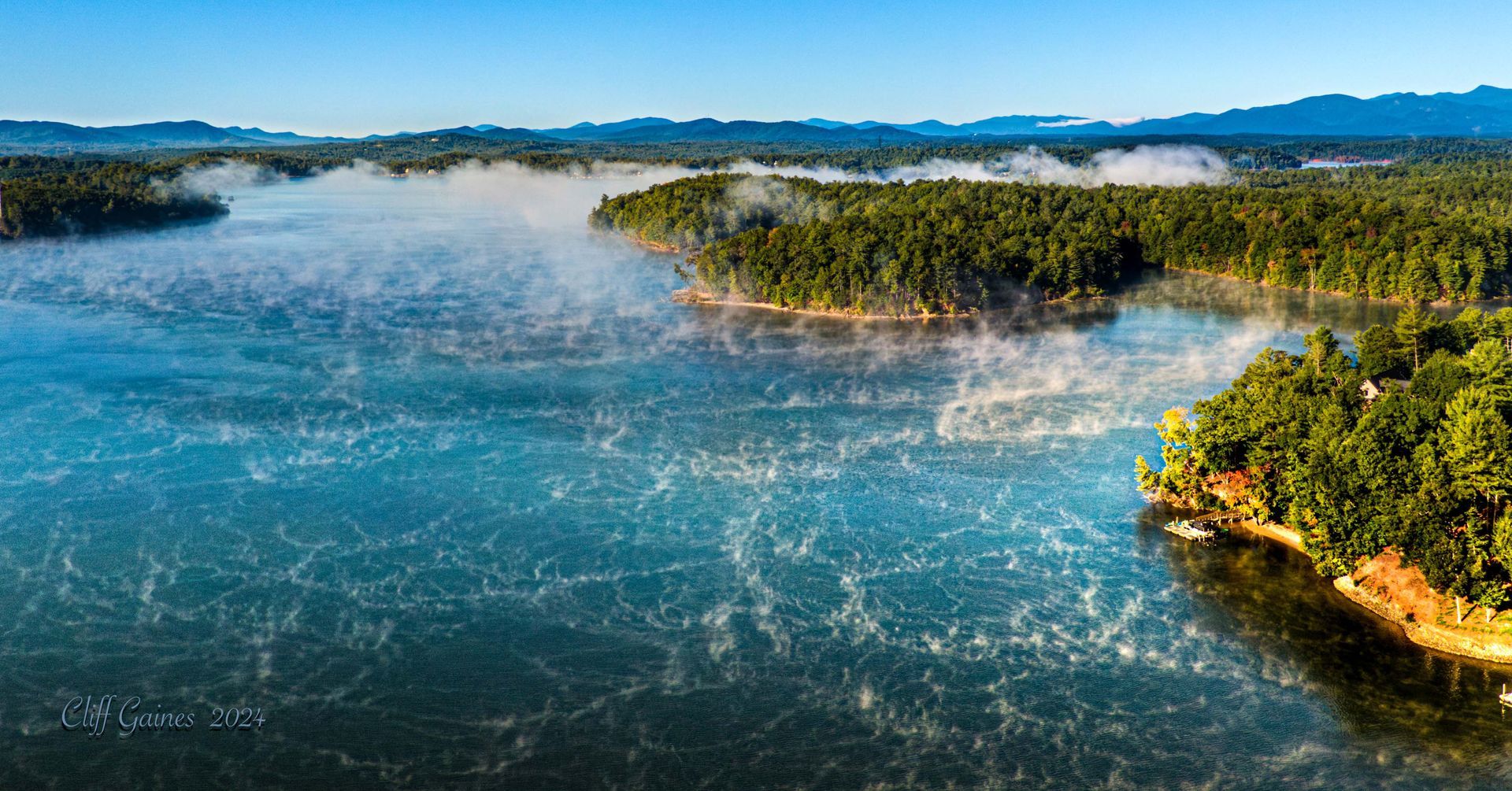 An aerial view of a lake surrounded by trees on a foggy day.