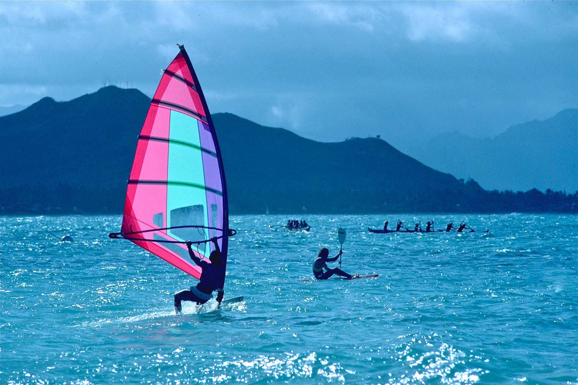 A person is windsurfing in the ocean with mountains in the background.