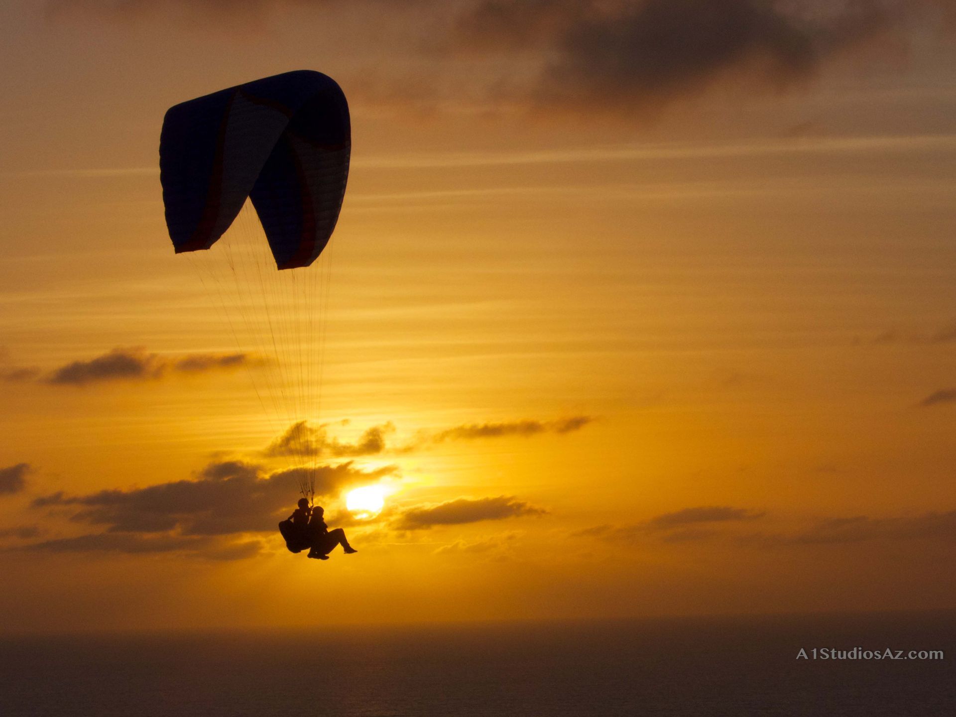 A person is parasailing in the sky at sunset