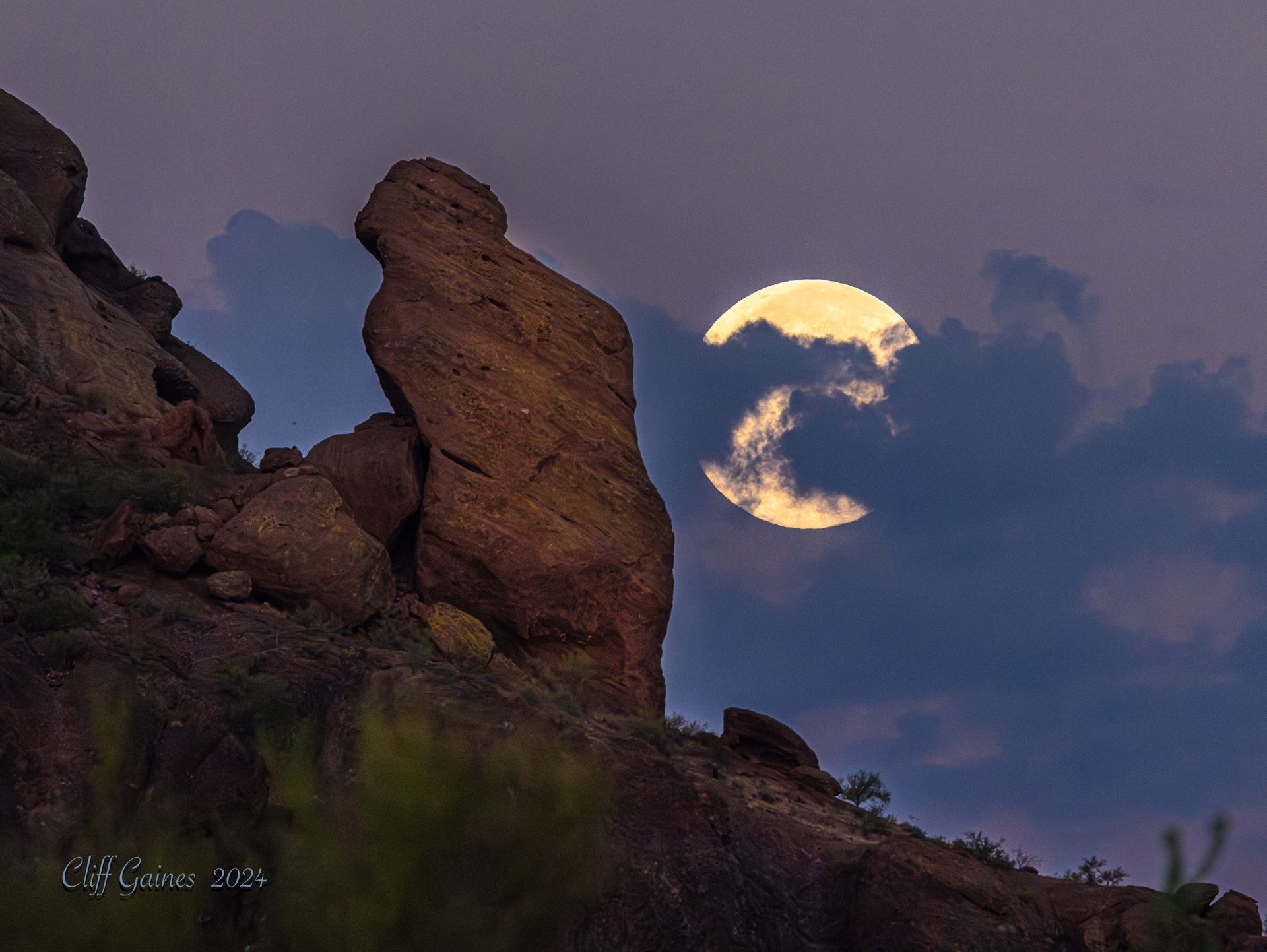 A full moon is rising over a rock formation