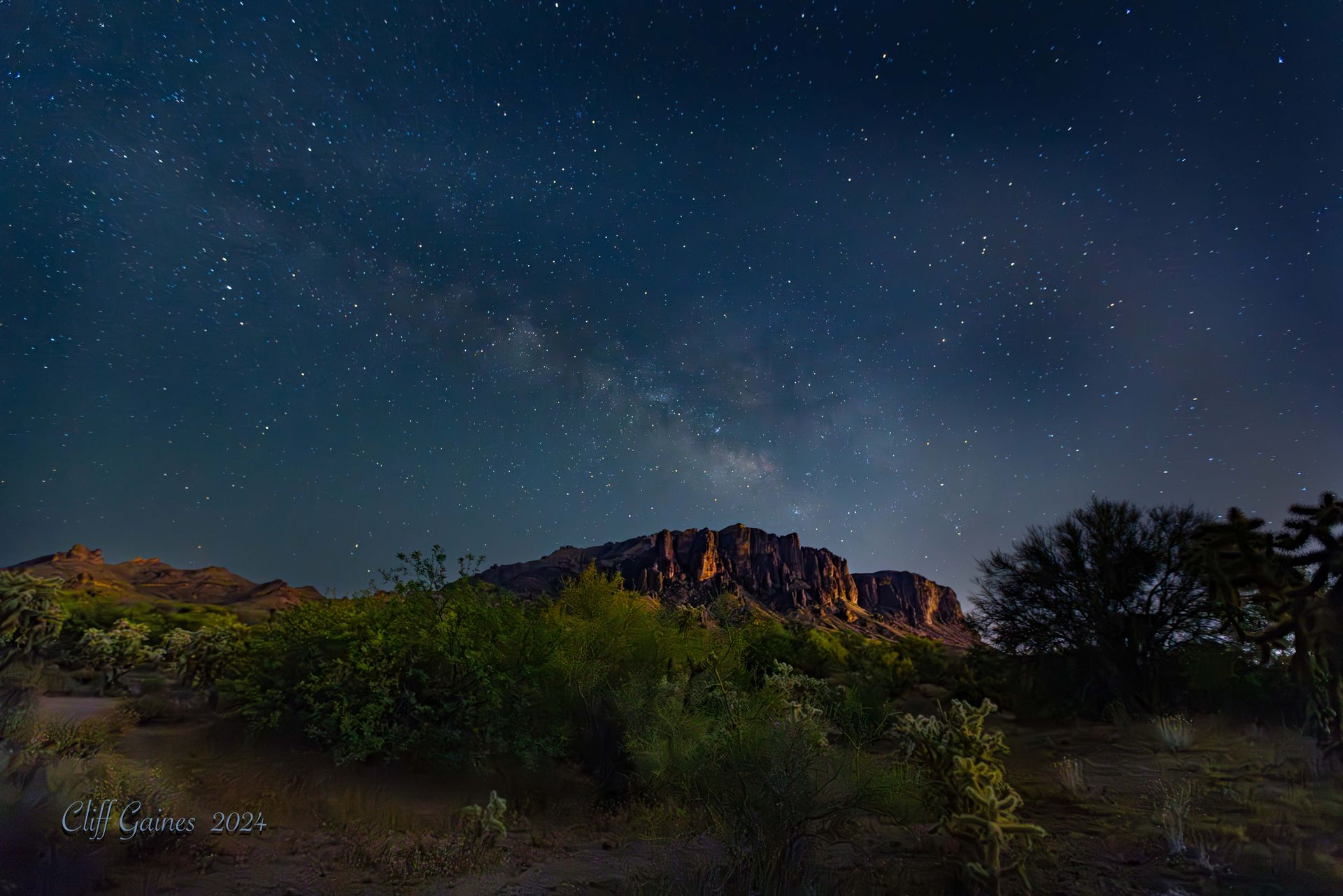 A night sky filled with lots of stars and a mountain in the background.