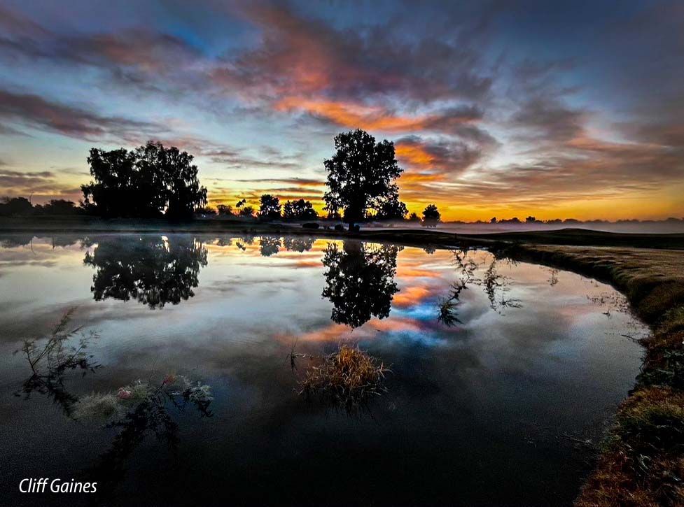 A sunset over a lake with trees reflected in the water