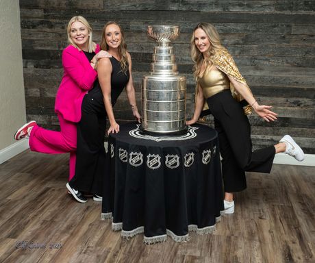 Three women are posing for a picture in front of a trophy.