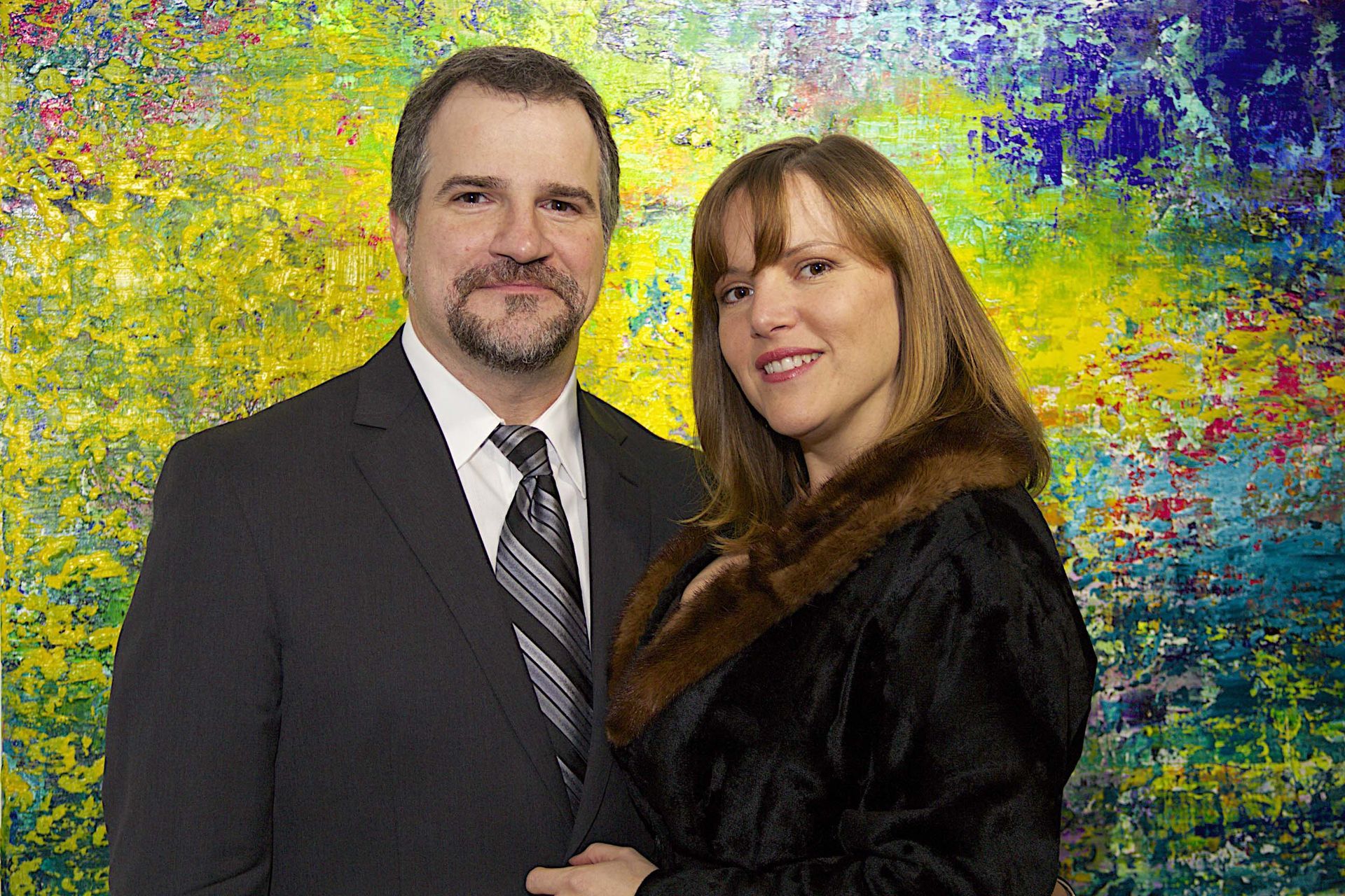 A man and a woman are posing for a picture in front of a colorful painting.