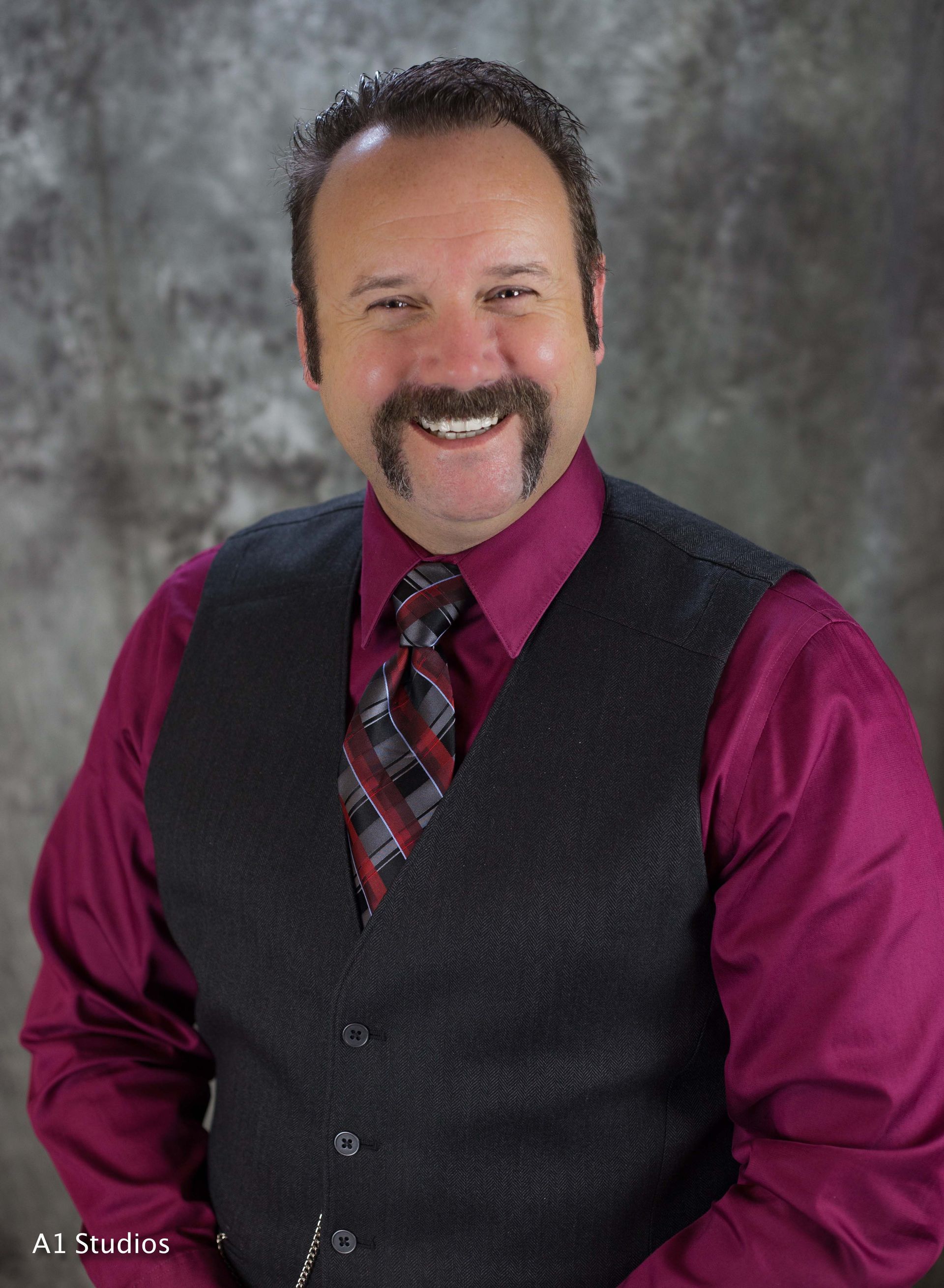 A man with a mustache is wearing a vest and tie