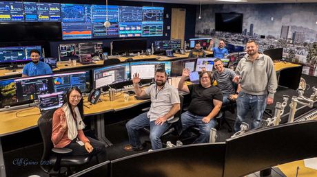 A group of people are posing for a picture in a control room.