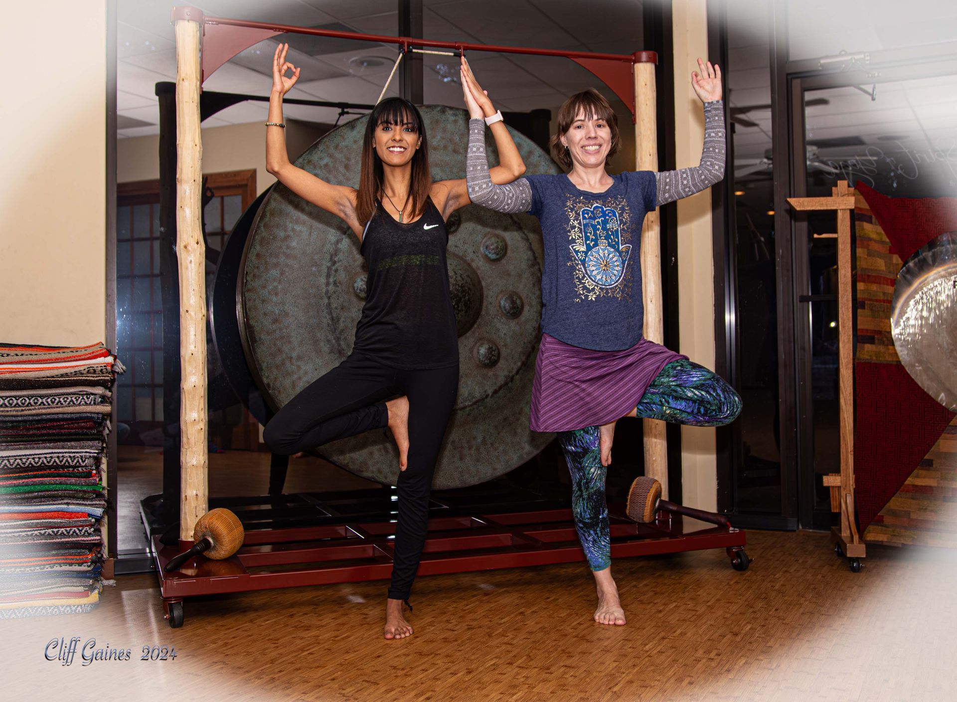 Two women are practicing yoga in front of a large gong
