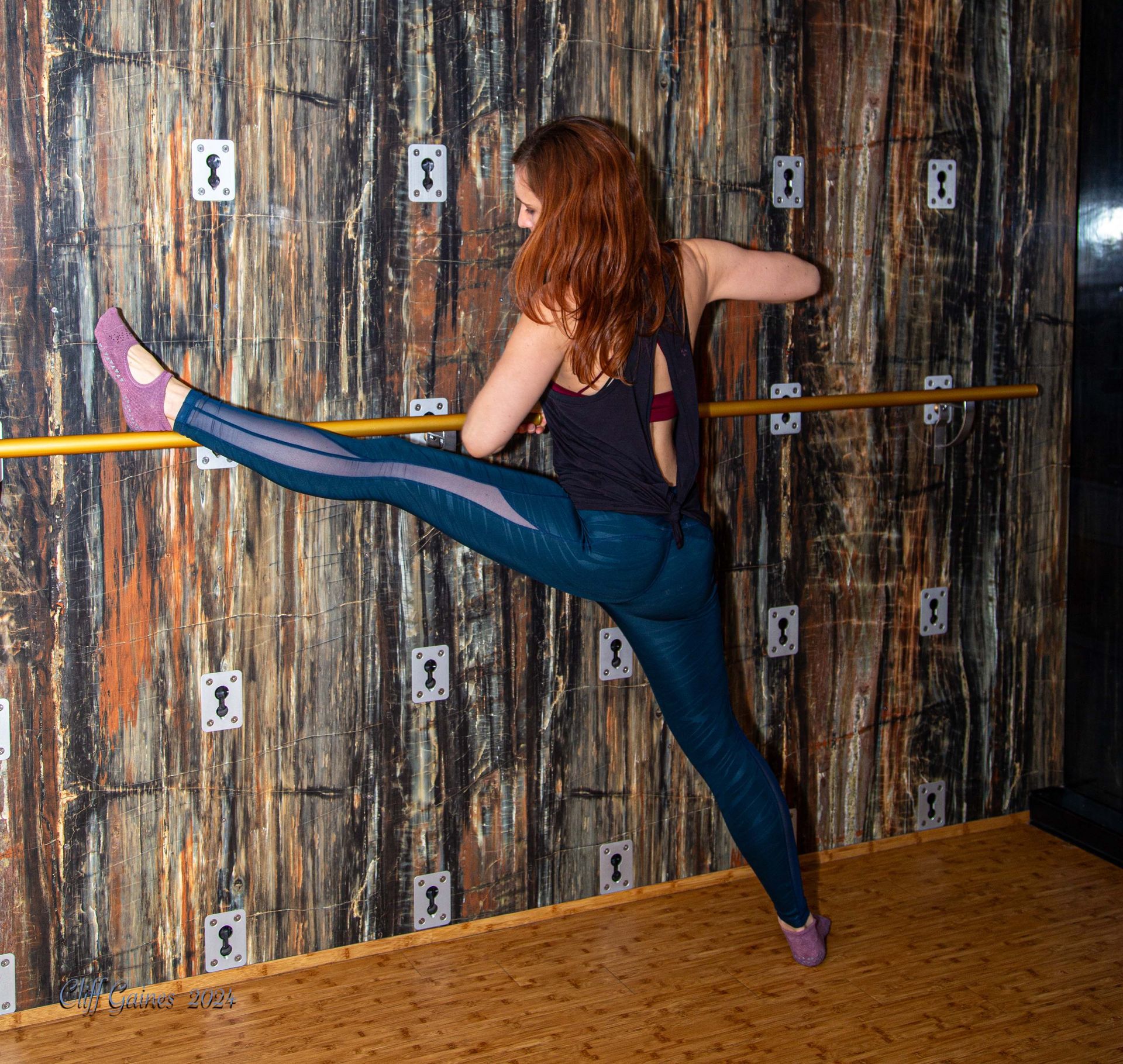 A woman is doing a split in front of a wooden wall