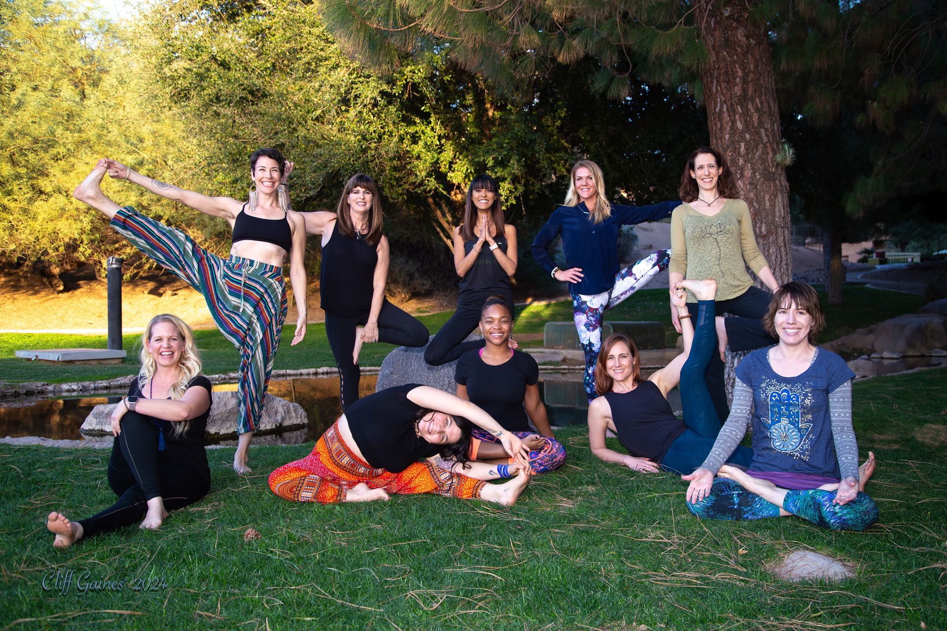 A group of women are posing for a picture while doing yoga in a park.