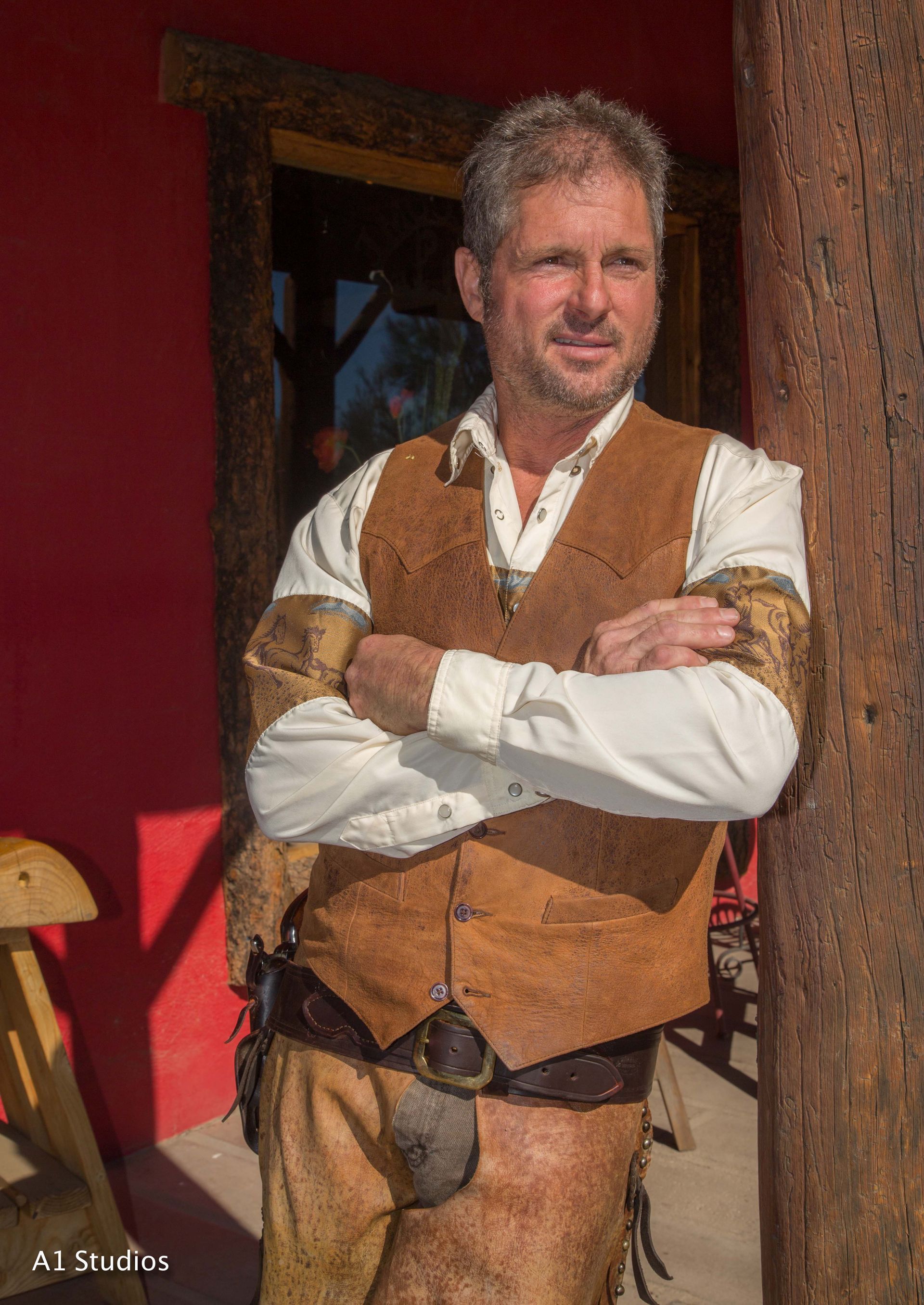 A man in a brown vest and white shirt is standing with his arms crossed.