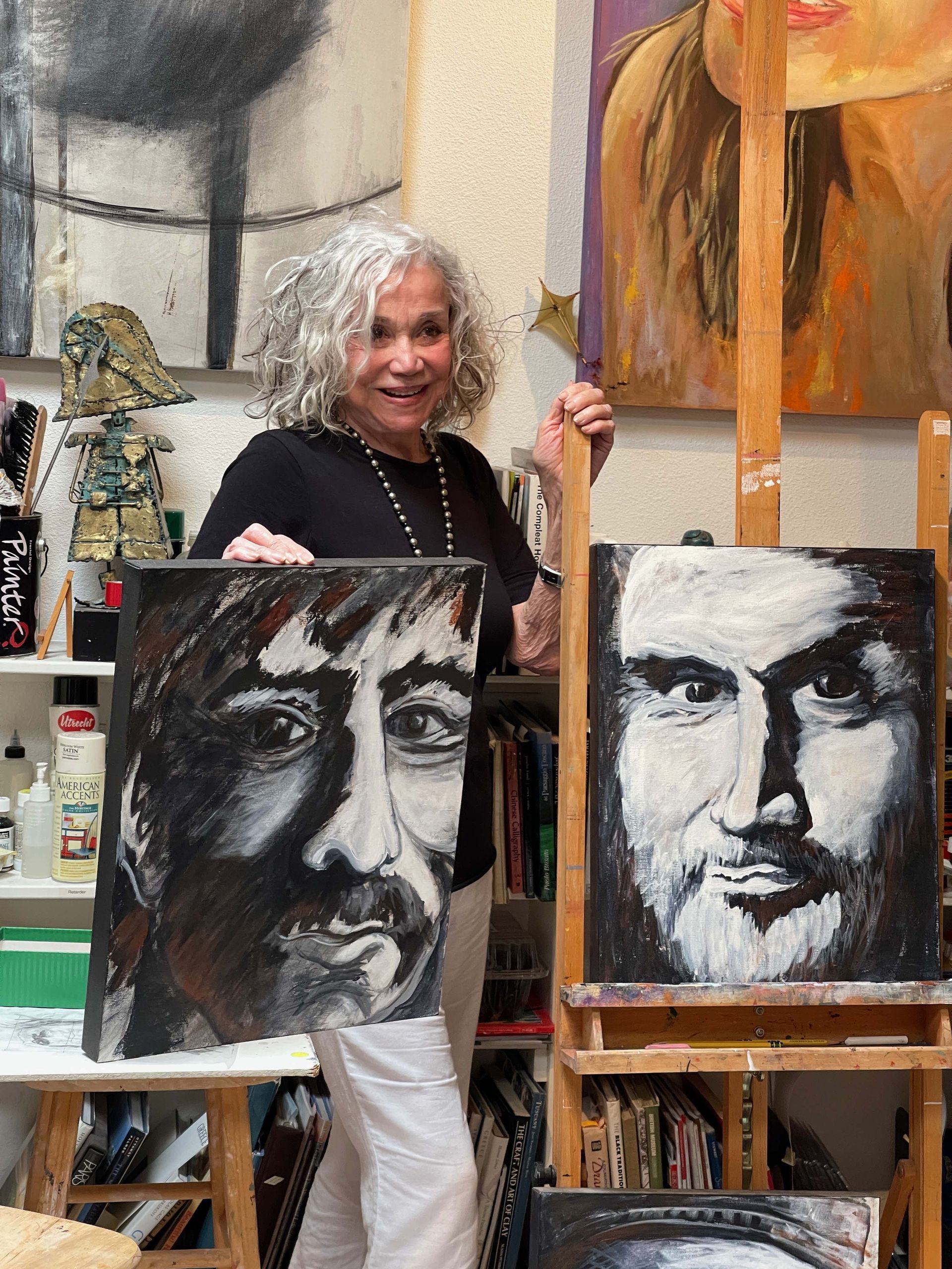 A woman is holding two paintings of a man 's face