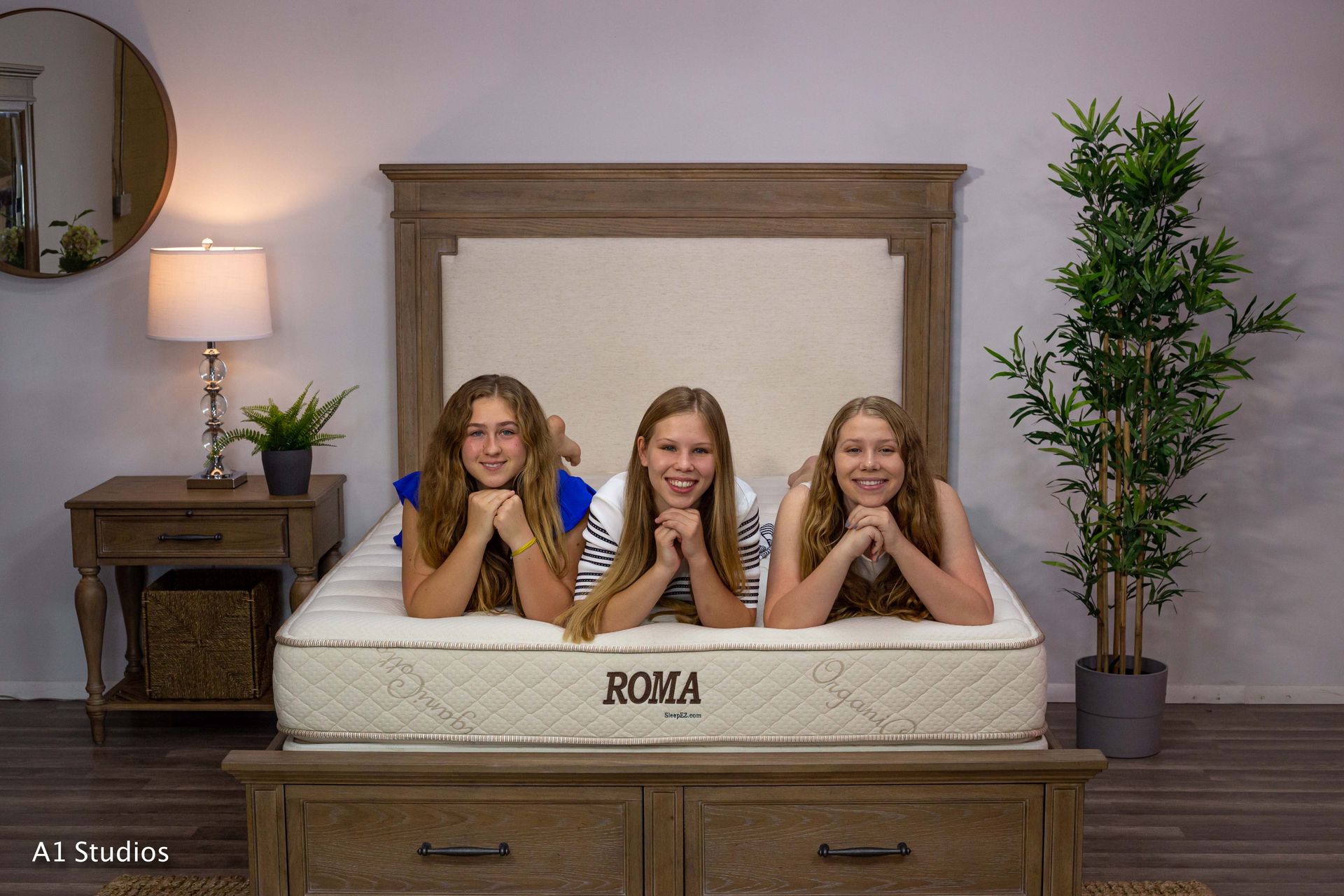 Three young girls are laying on a mattress in a bedroom.