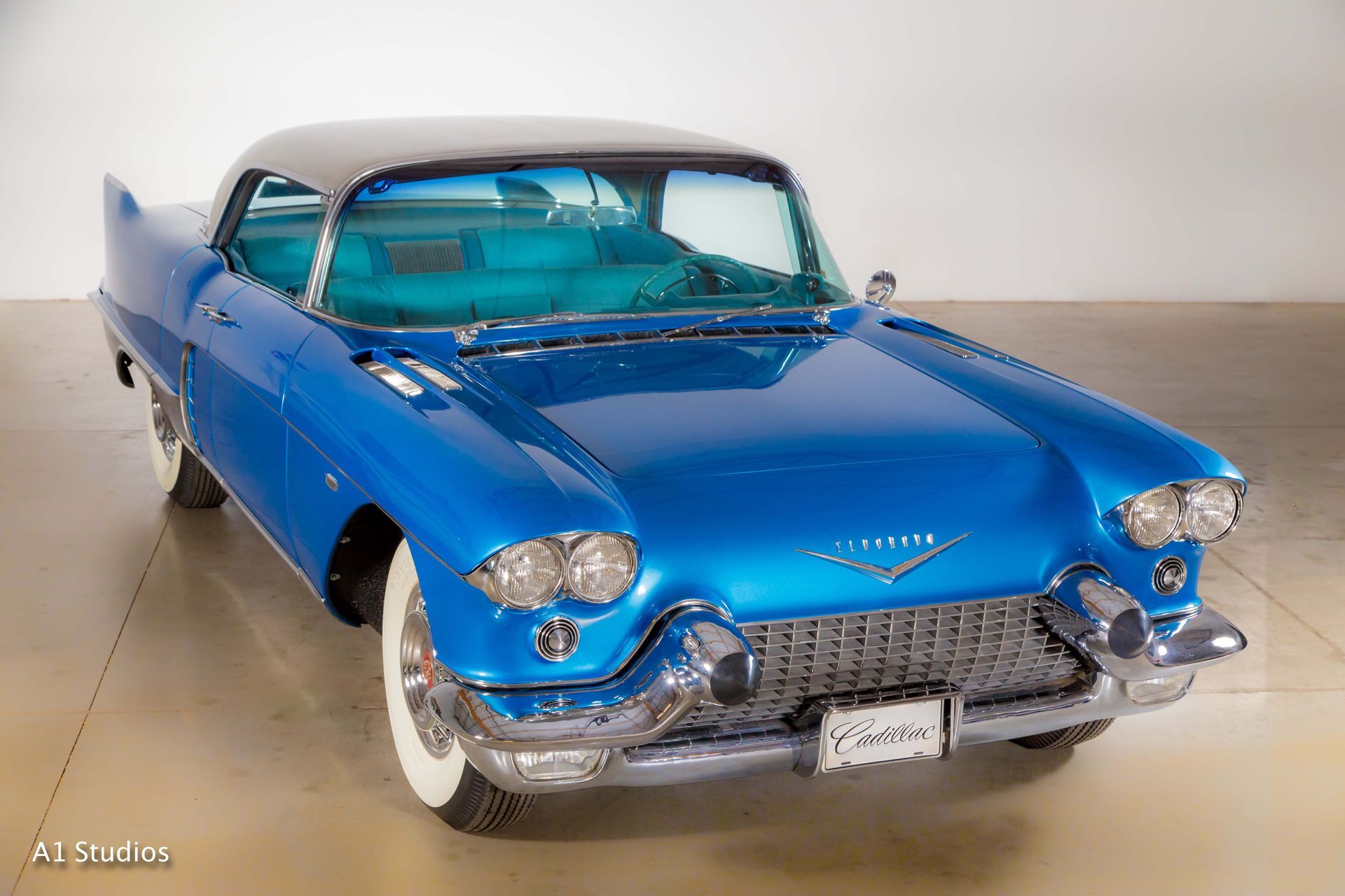 A blue cadillac with white tires is parked in a garage.