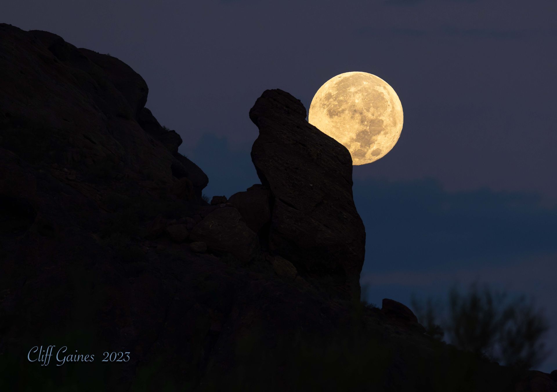A full moon is rising over a rock formation