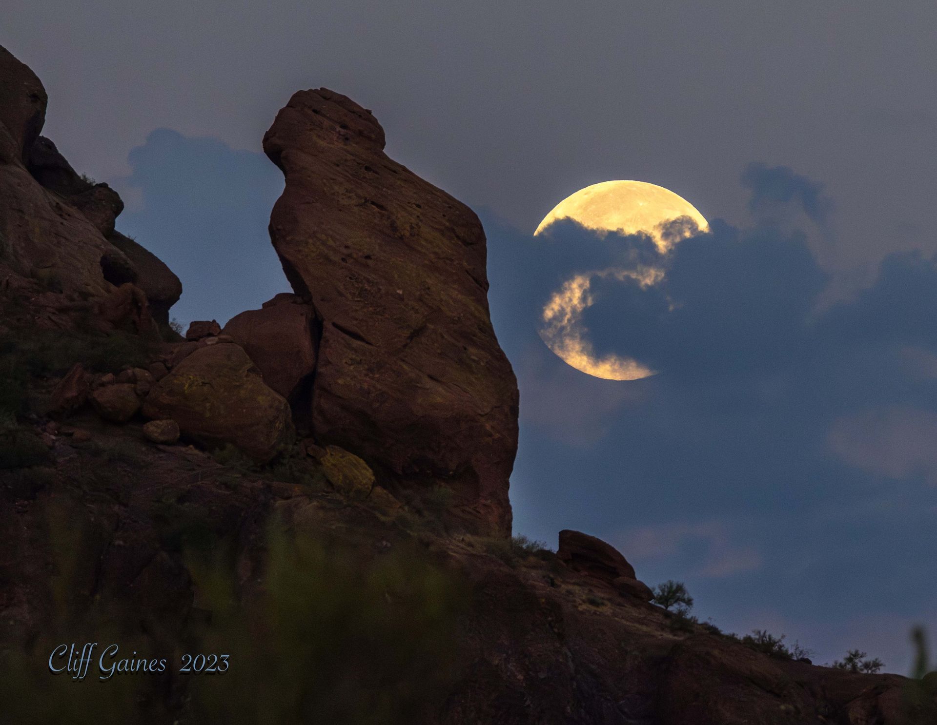 A full moon is rising over a rock formation