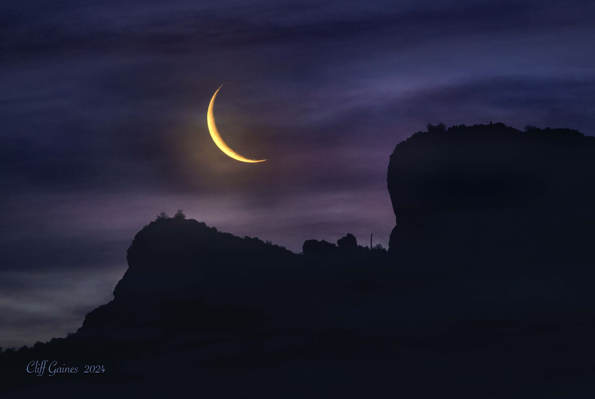 A crescent moon is rising over a mountain at night.