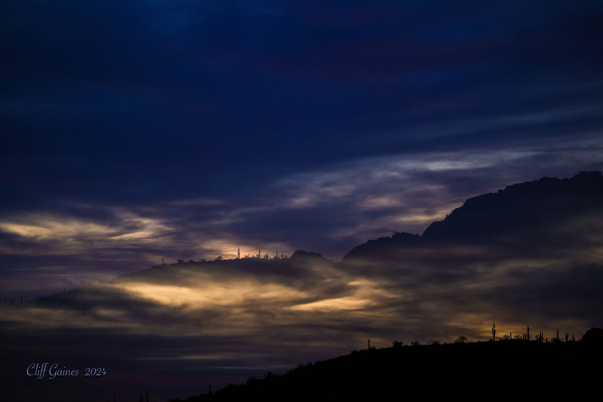 A mountain silhouetted against a cloudy sky at sunset.