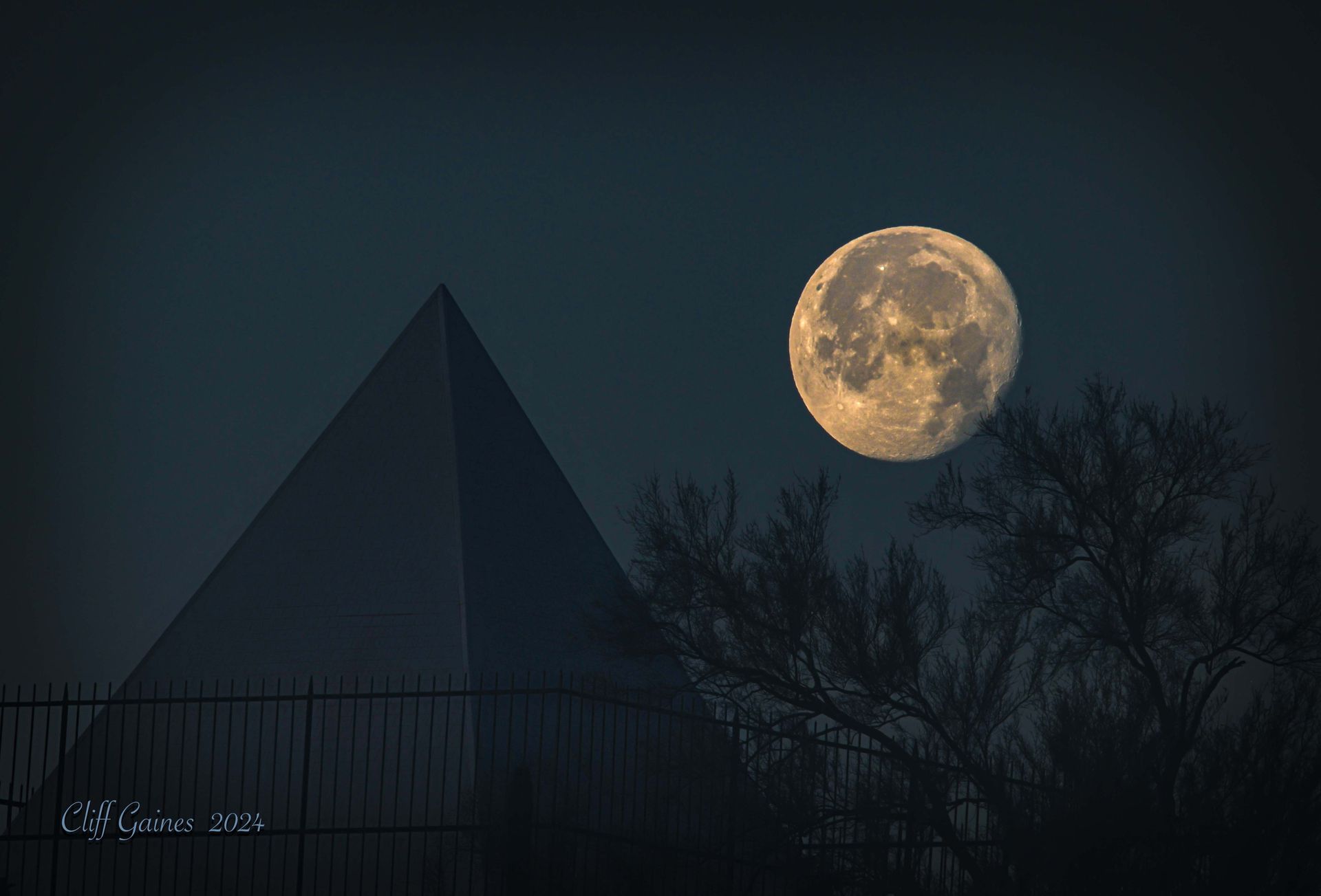 A full moon rises over a pyramid and trees