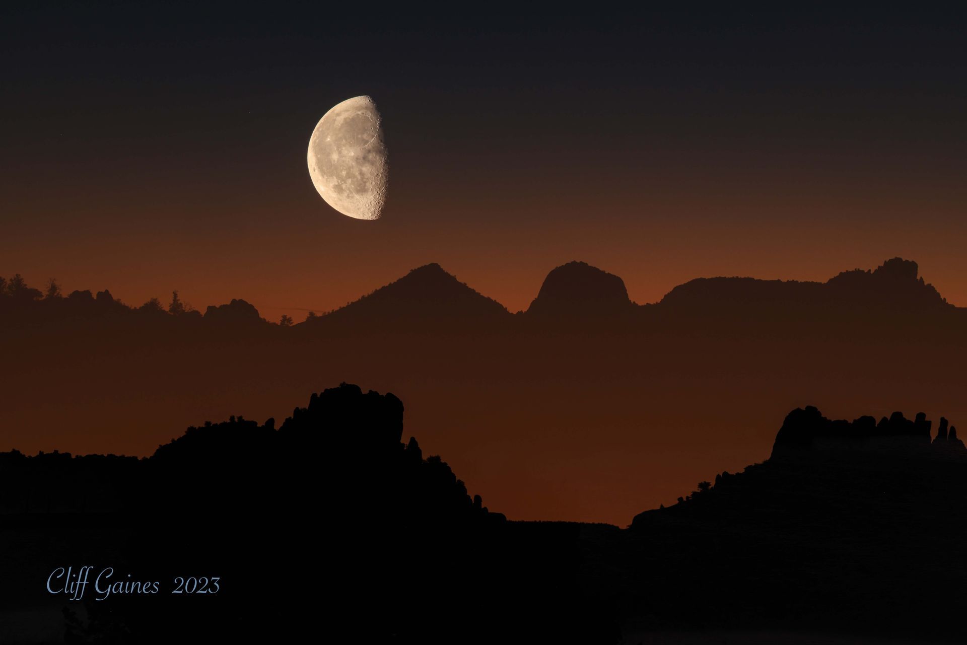 A silhouette of mountains with a crescent moon in the sky