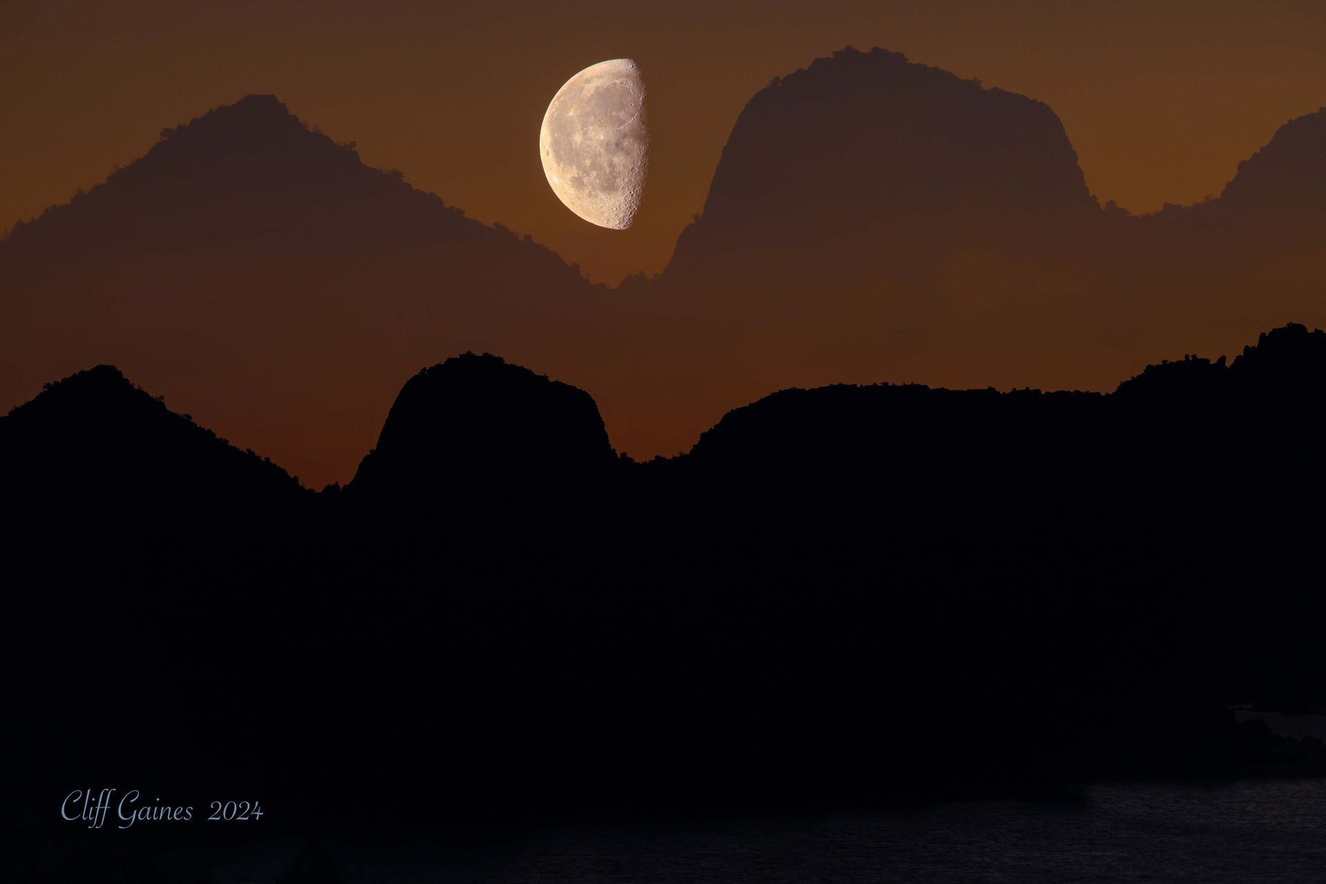 A crescent moon is rising over a mountain range