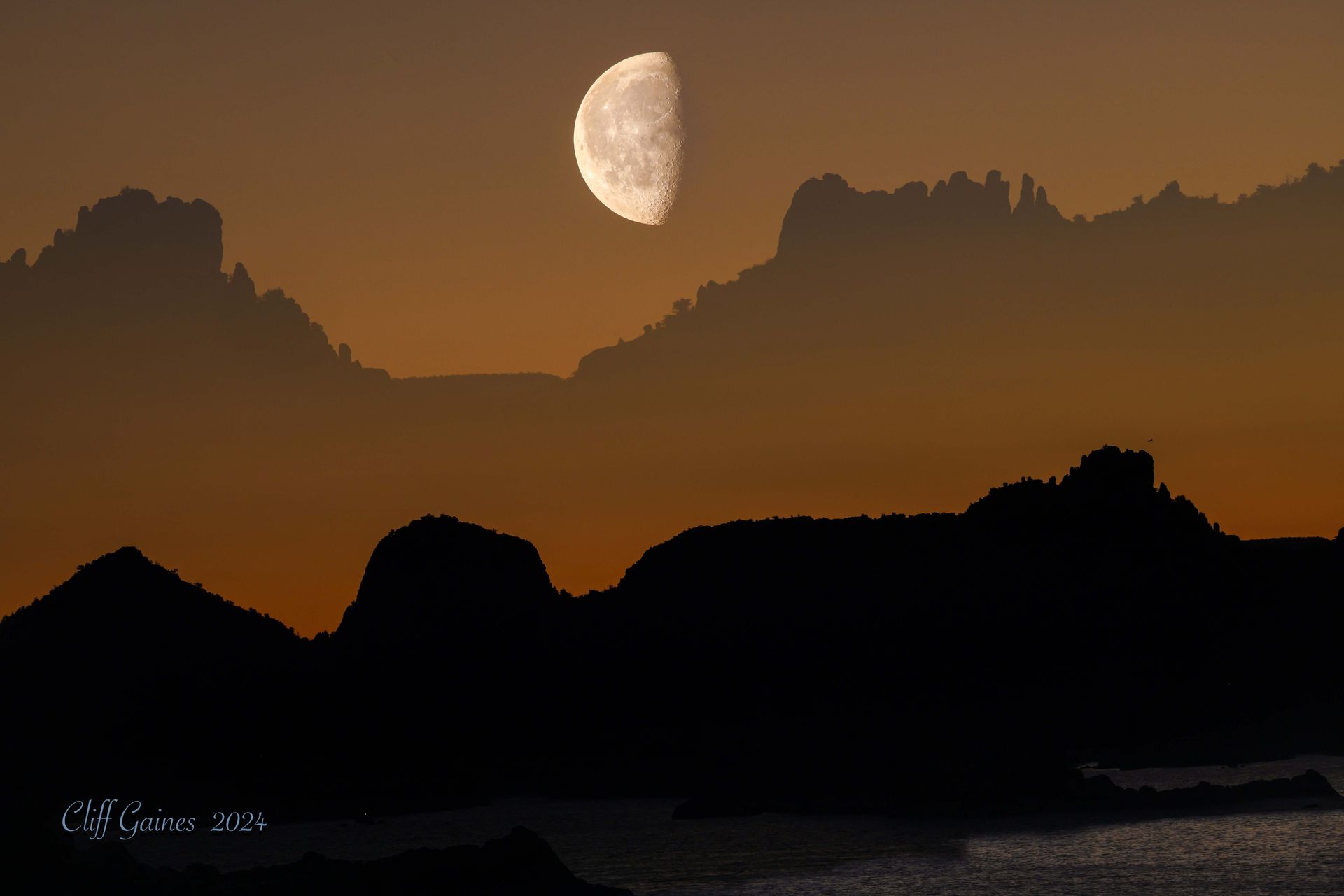 A crescent moon is rising over a body of water