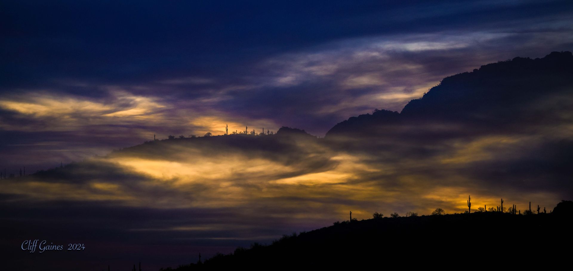 A mountain silhouetted against a cloudy sky at sunset.