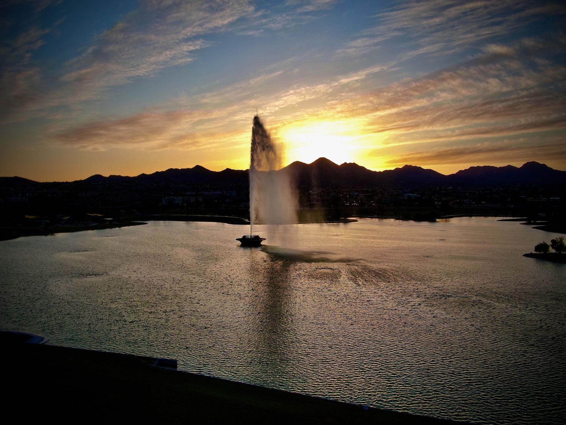 A fountain in the middle of a lake at sunset