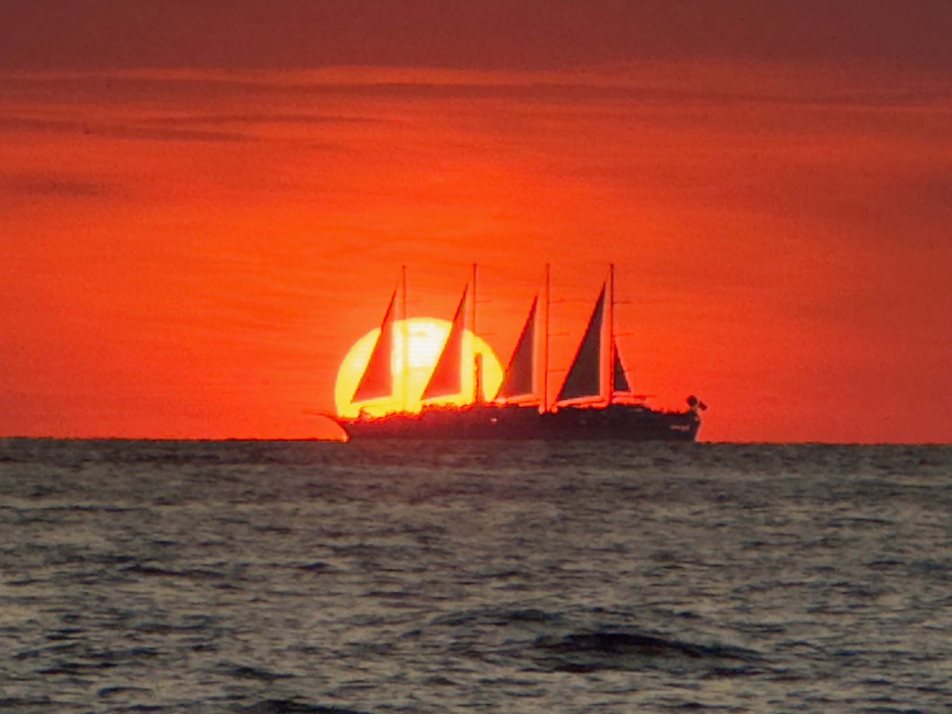 A sailboat is sailing in the ocean at sunset.