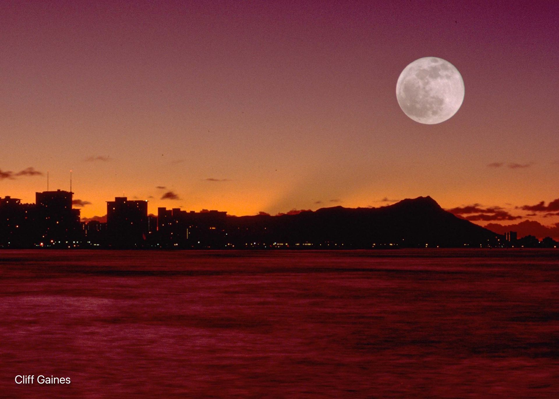 A full moon rises over a city at sunset