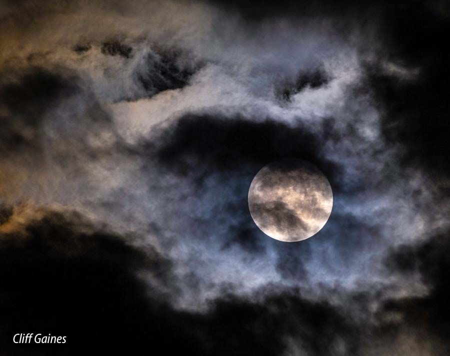 A full moon is visible through the clouds in the night sky.